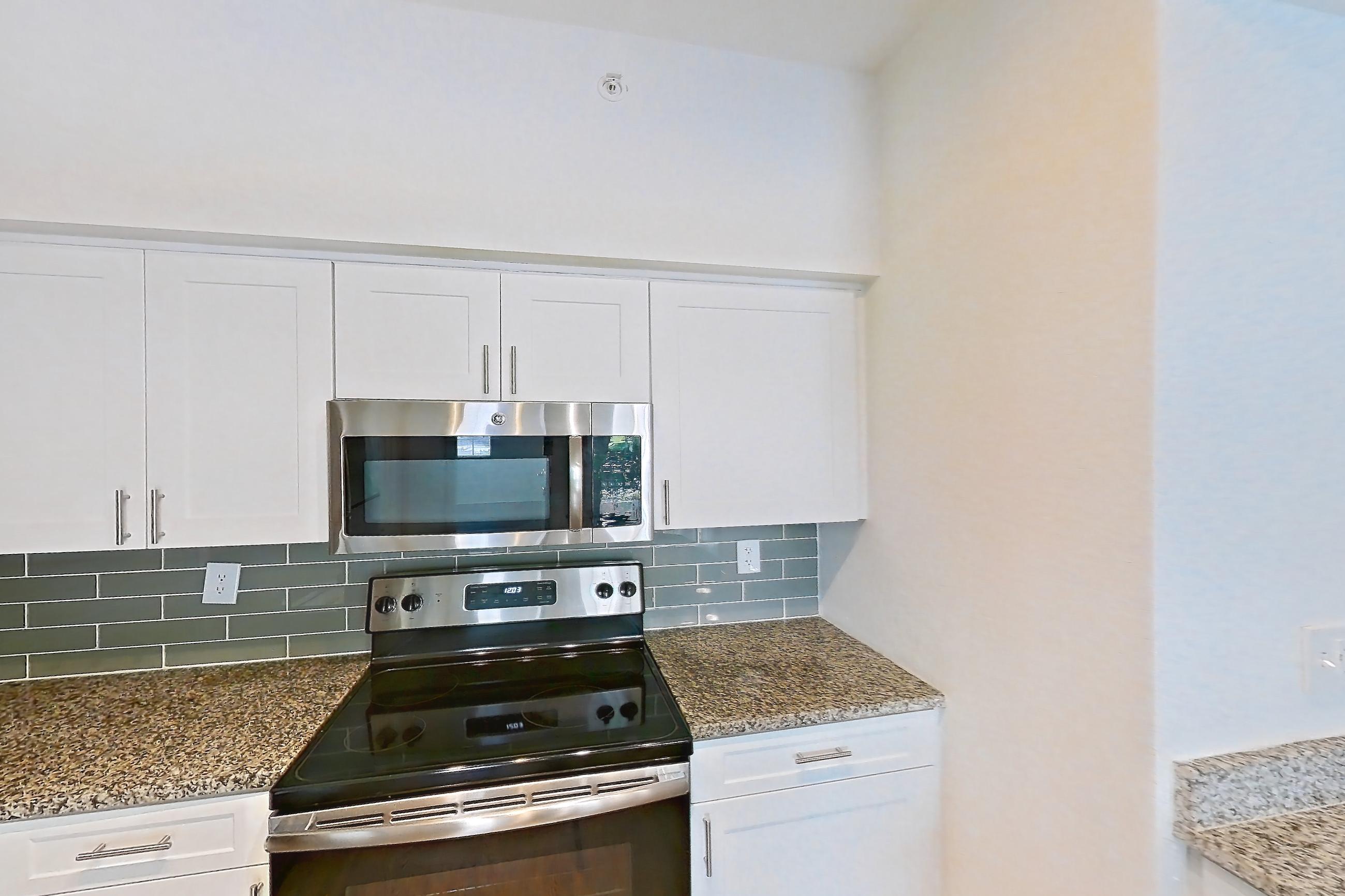 Kitchen with dark wood-finish flooring, dishwasher, electric range, light stone countertops, light wood-finish flooring, microwave, oven/range, refrigerator, and stainless steel appliances, Apartment 08-110 at Solano at Miramar
