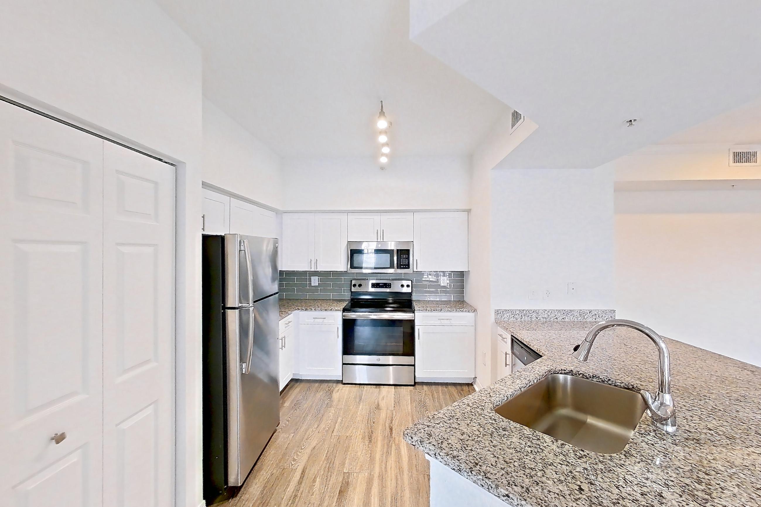 Kitchen entryway with dark wood-finish flooring, dishwasher, electric range, light stone countertops, light wood-finish flooring, oven/range, refrigerator, and stainless steel appliances, Apartment 08-310 at Solano at Miramar