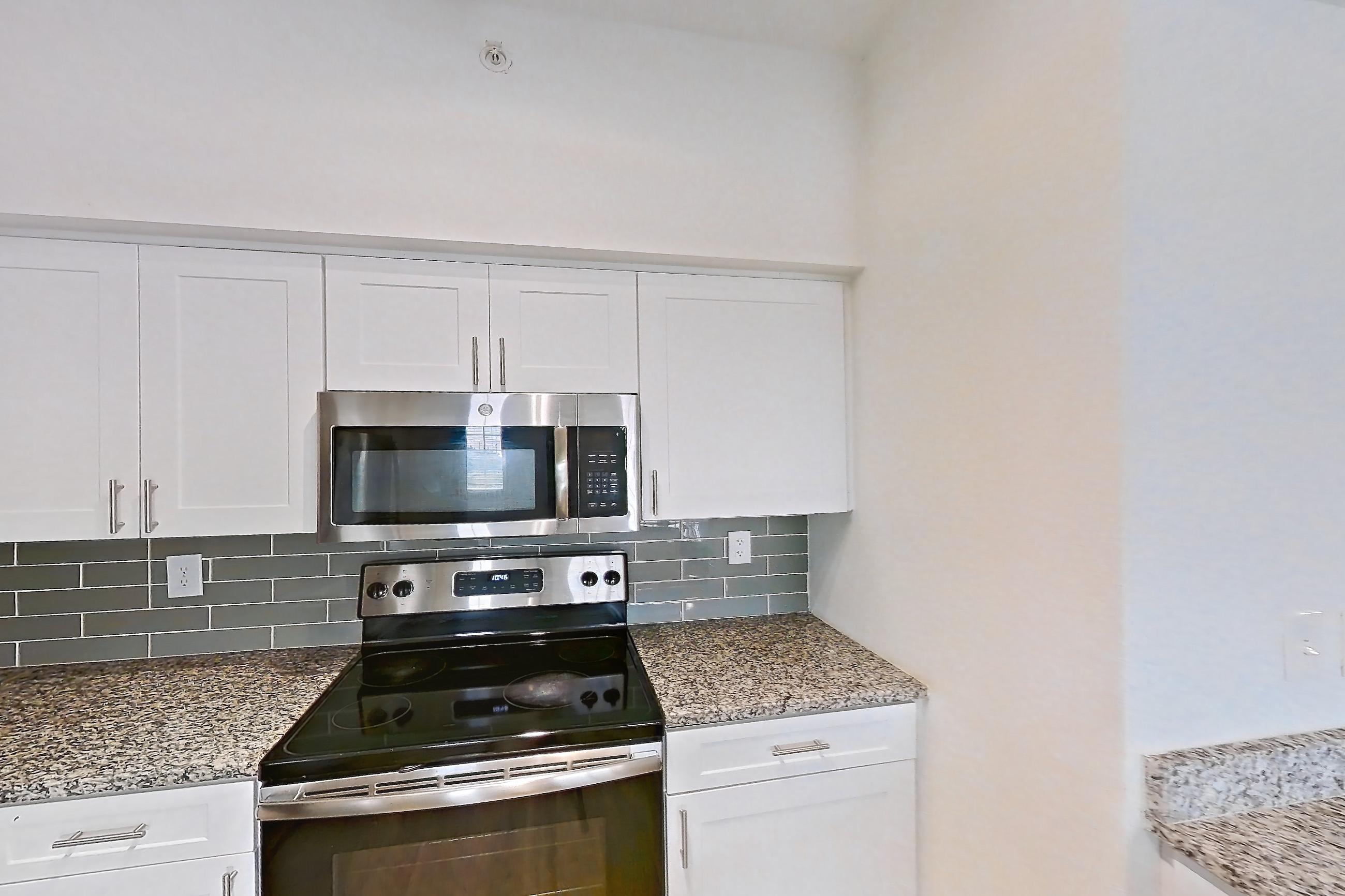 Kitchen with dark wood-finish flooring, dishwasher, electric range, light stone countertops, light wood-finish flooring, microwave, oven/range, refrigerator, and stainless steel appliances, Apartment 08-310 at Solano at Miramar