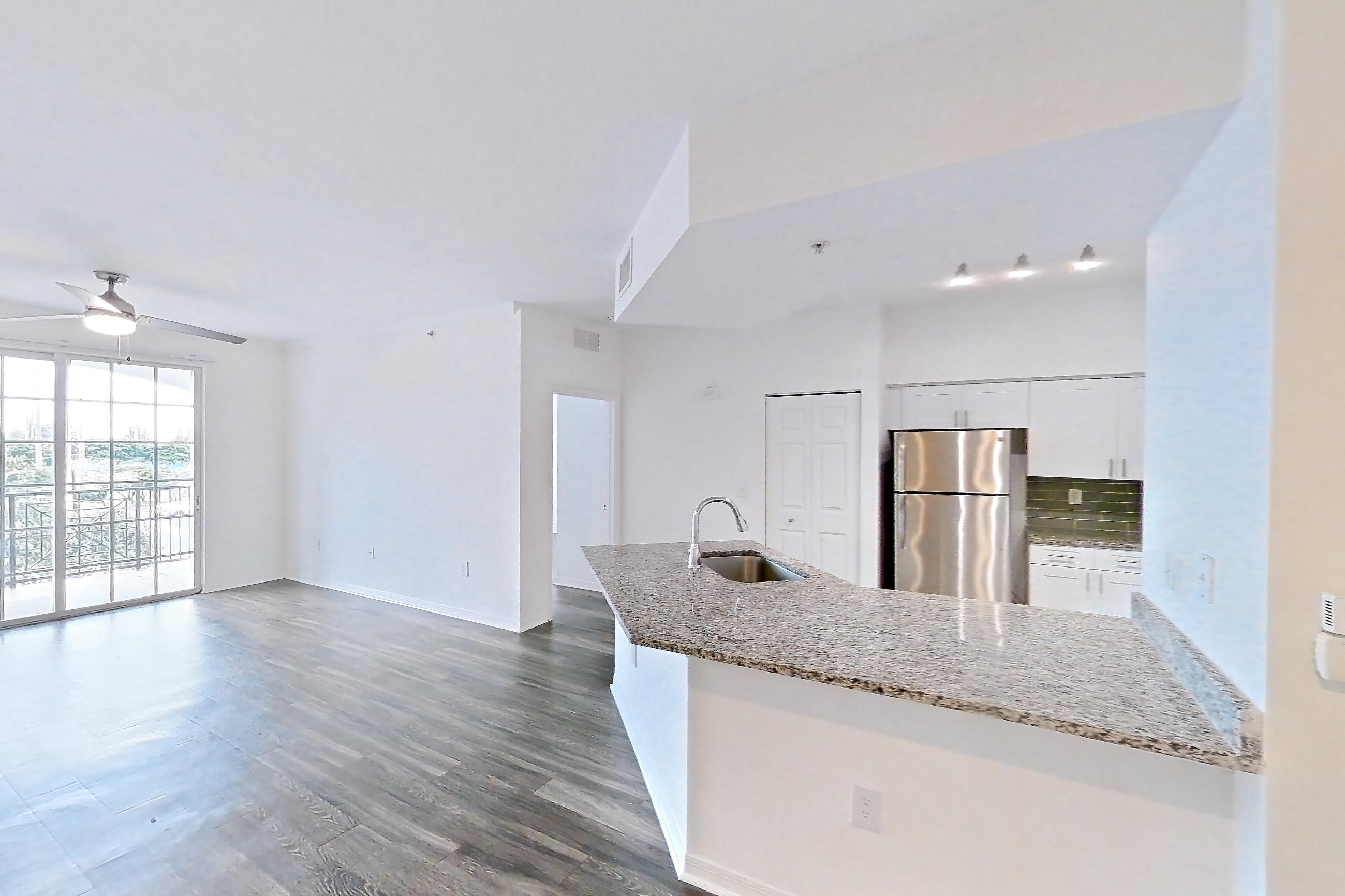 Living space with dark wood-finish flooring, light stone countertops, refrigerator, and stainless steel appliances, Apartment 08-310 at Solano at Miramar
