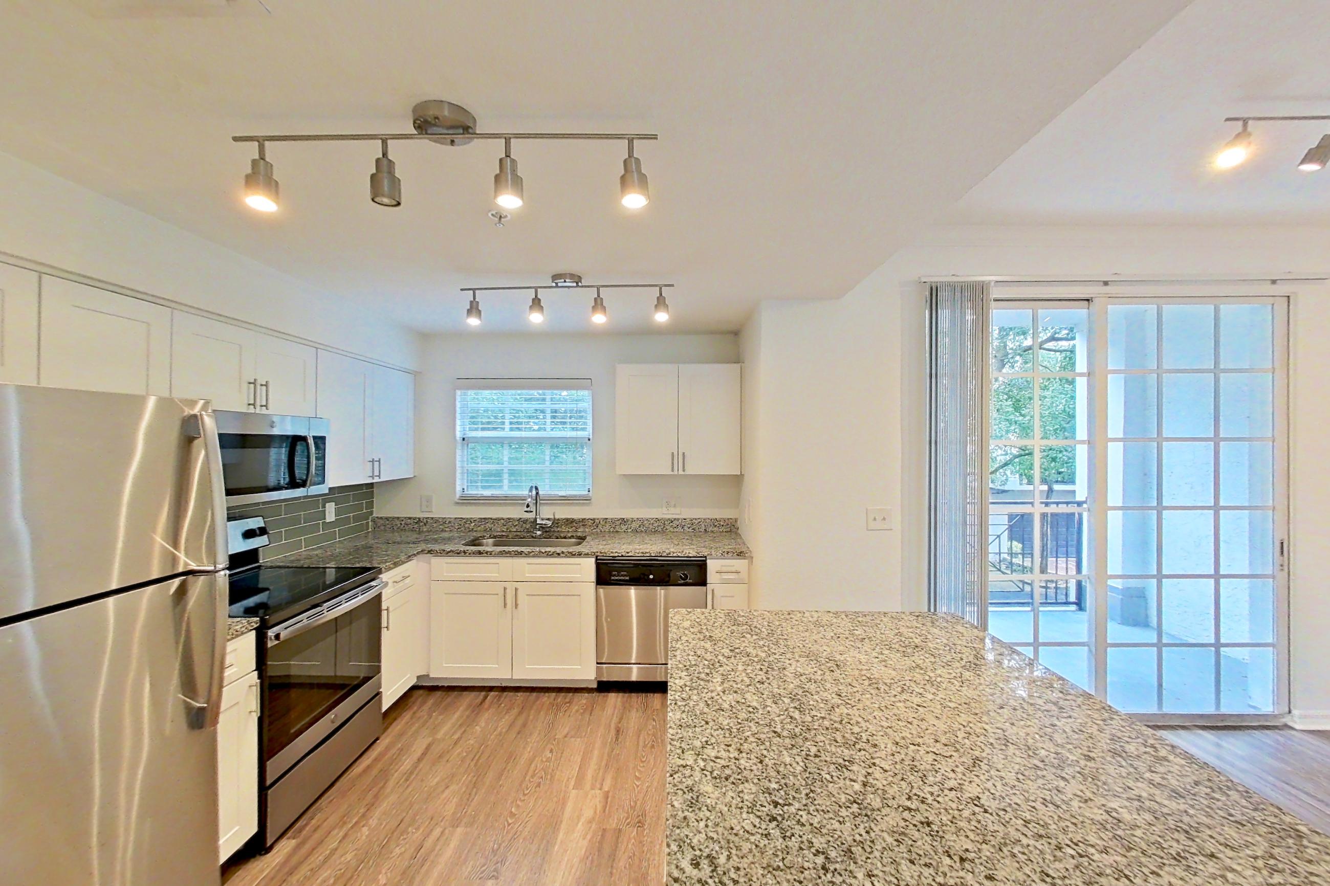 Kitchen entryway with dark wood-finish flooring, dishwasher, electric range, light stone countertops, light wood-finish flooring, microwave, oven/range, refrigerator, stainless steel appliances, and white appliances, Apartment 16-02573 at Solano at Miramar