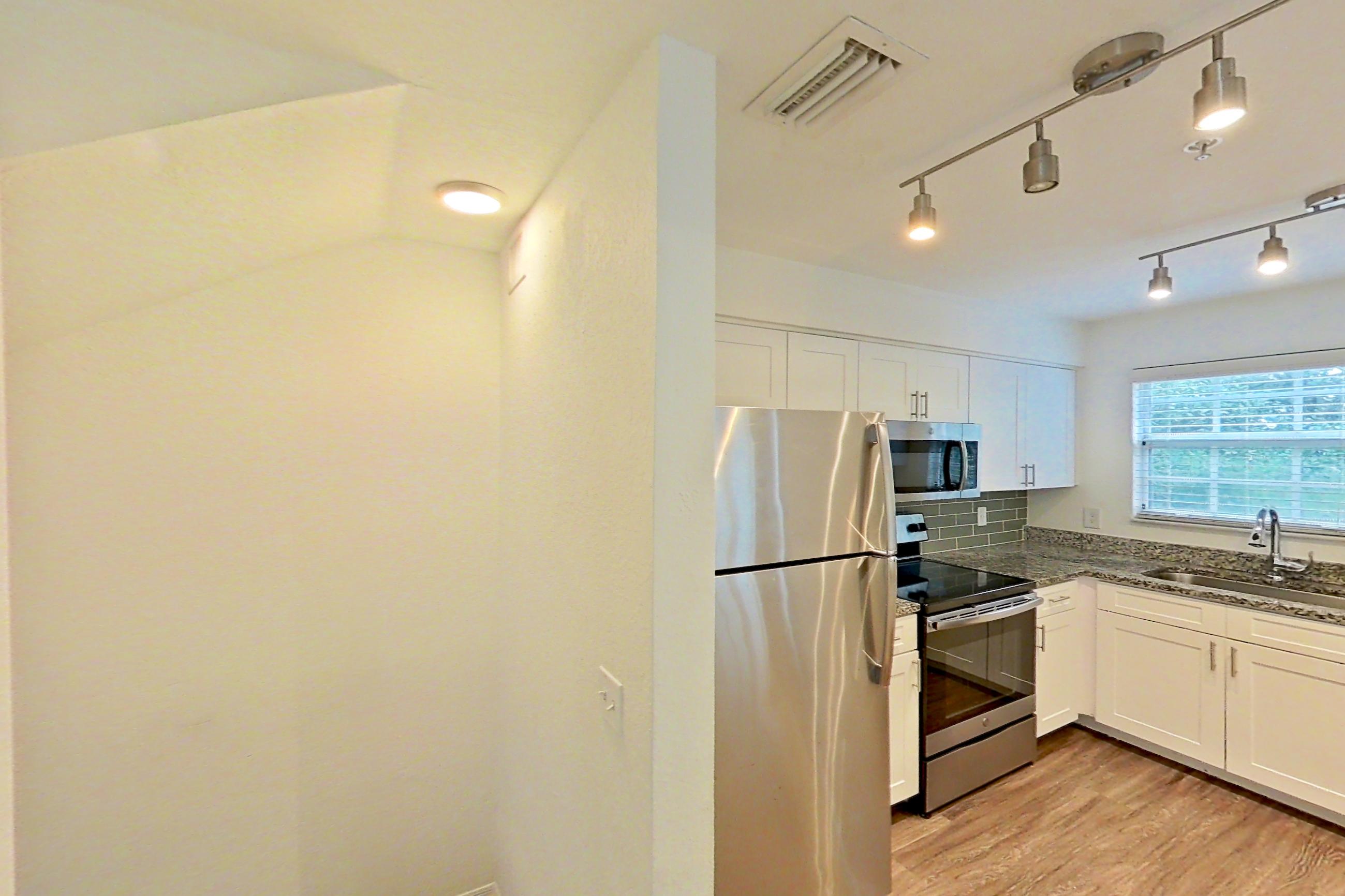 Kitchen entryway with dark wood-finish flooring, dishwasher, electric range, light stone countertops, light wood-finish flooring, microwave, oven/range, refrigerator, stainless steel appliances, and white appliances, Apartment 16-02573 at Solano at Miramar