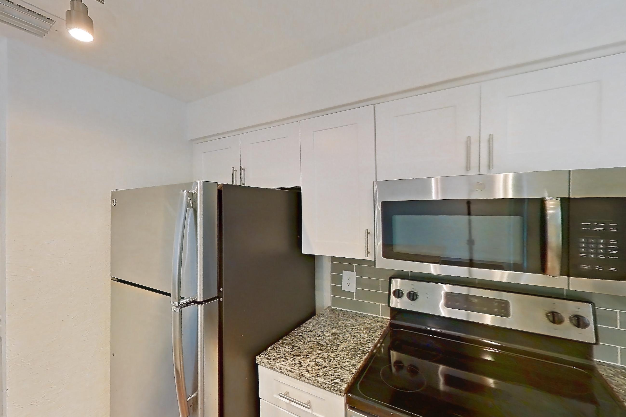 Kitchen with dark stone countertops, dishwasher, electric range, light countertops, light stone countertops, light wood-finish flooring, microwave, oven/range, and stainless steel appliances, Apartment 16-02573 at Solano at Miramar