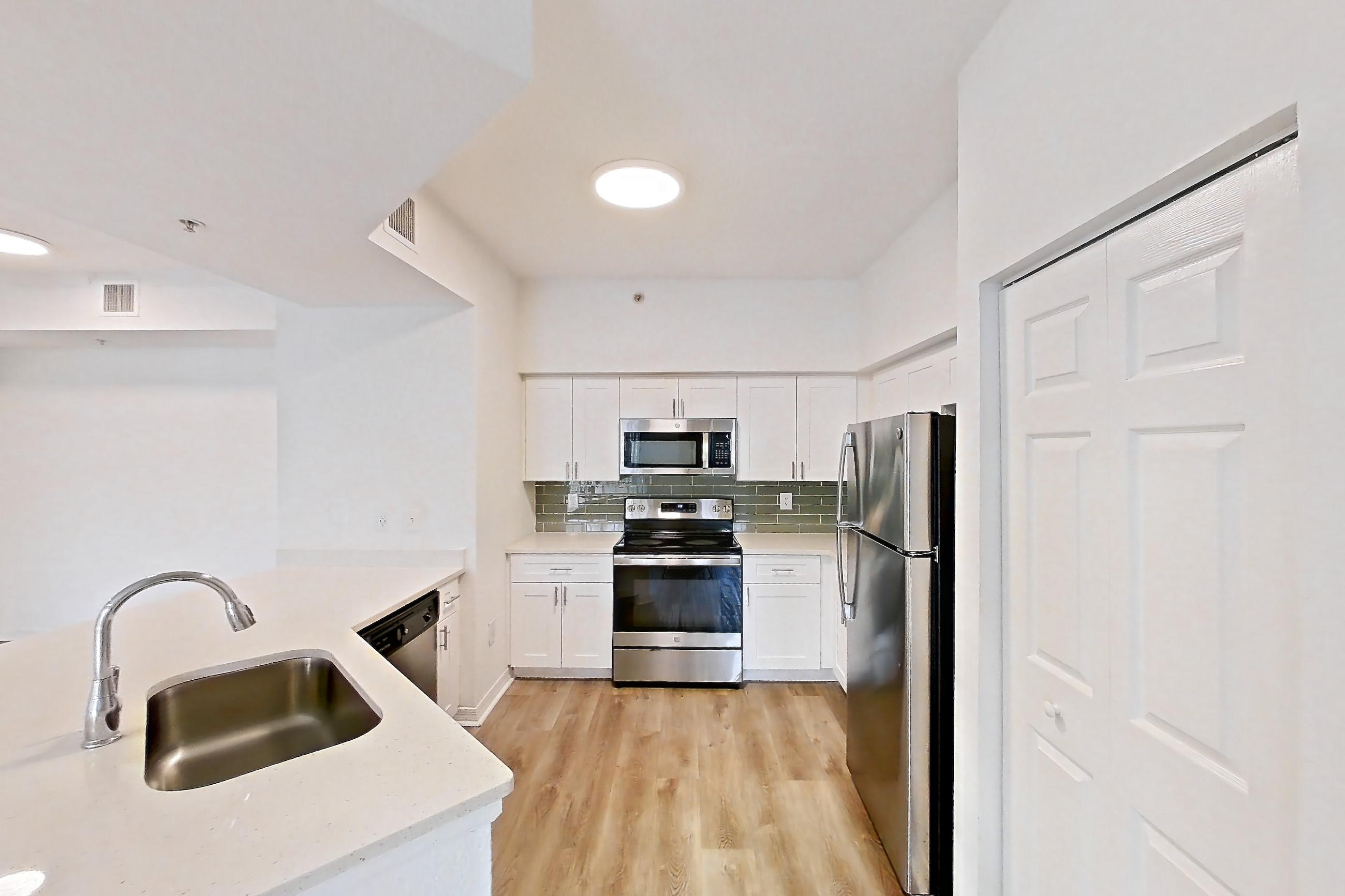 Kitchen entryway with dishwasher, electric range, light stone countertops, light wood-finish flooring, oven/range, refrigerator, and stainless steel appliances, Apartment 03-304 at Solano at Miramar