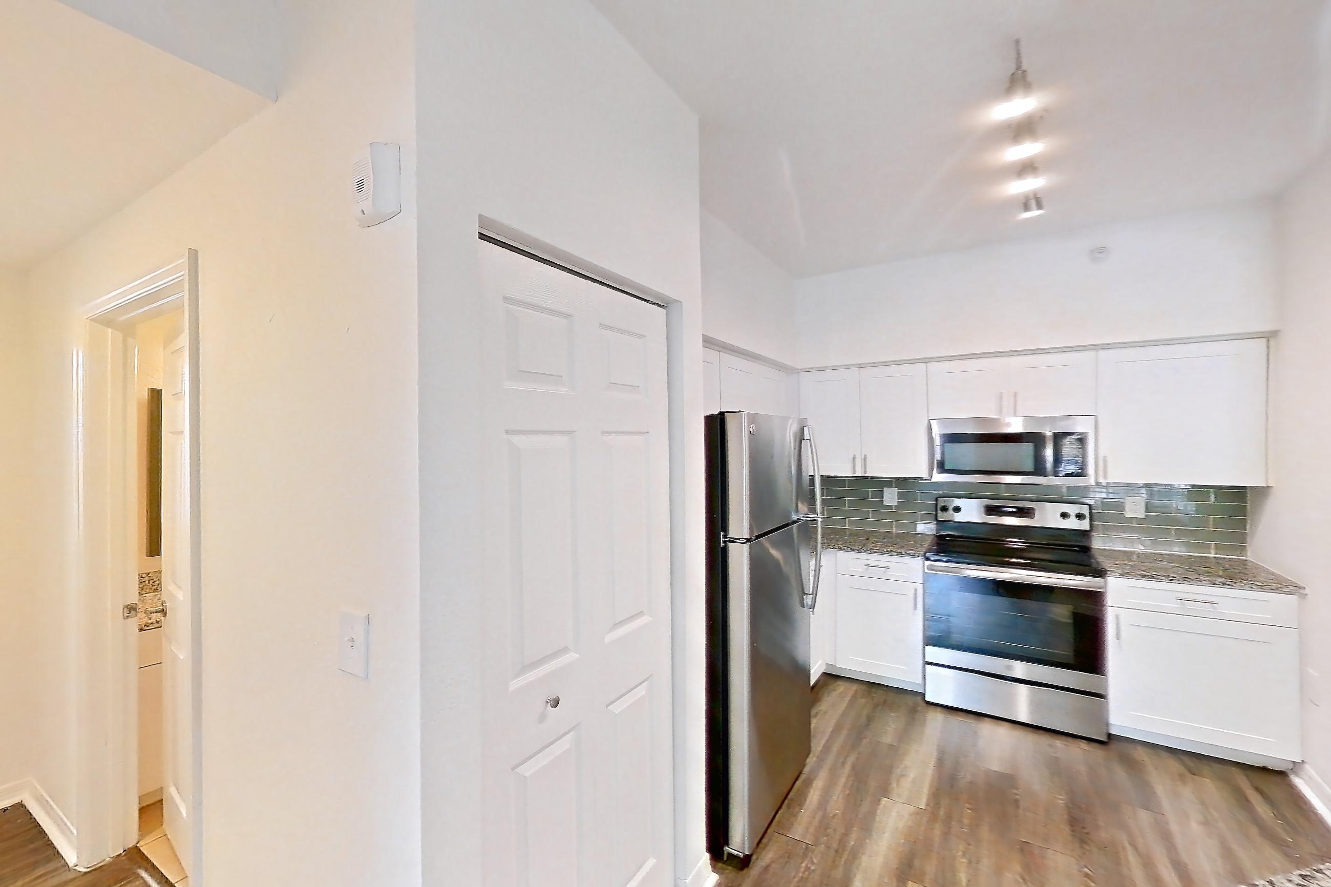 Kitchen entryway with dark wood-finish flooring, dishwasher, electric range, light stone countertops, oven/range, refrigerator, and stainless steel appliances, Apartment 04-205 at Solano at Miramar