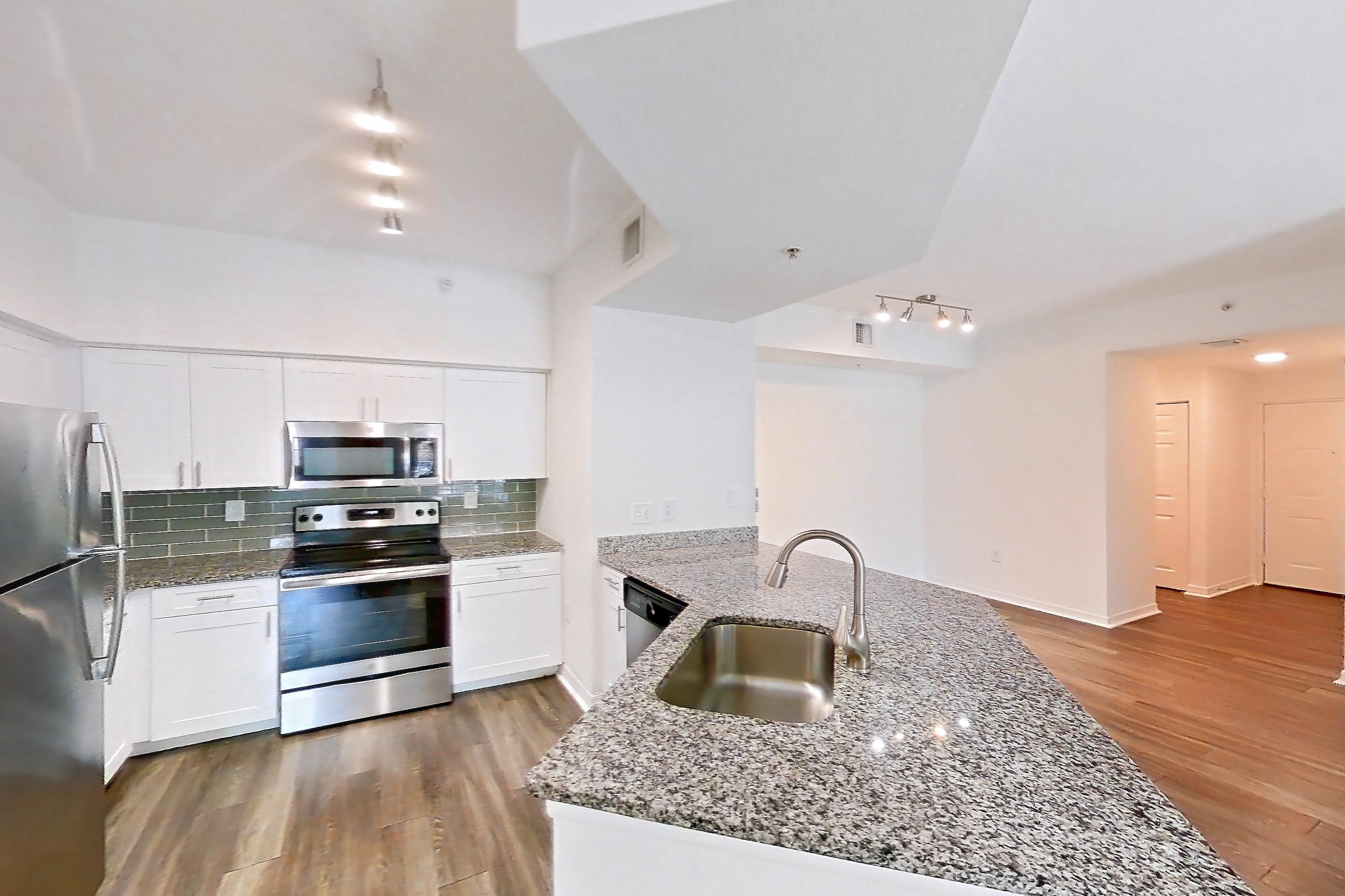 Kitchen entryway with dark wood-finish flooring, dishwasher, electric range, light stone countertops, oven/range, refrigerator, and stainless steel appliances, Apartment 04-205 at Solano at Miramar