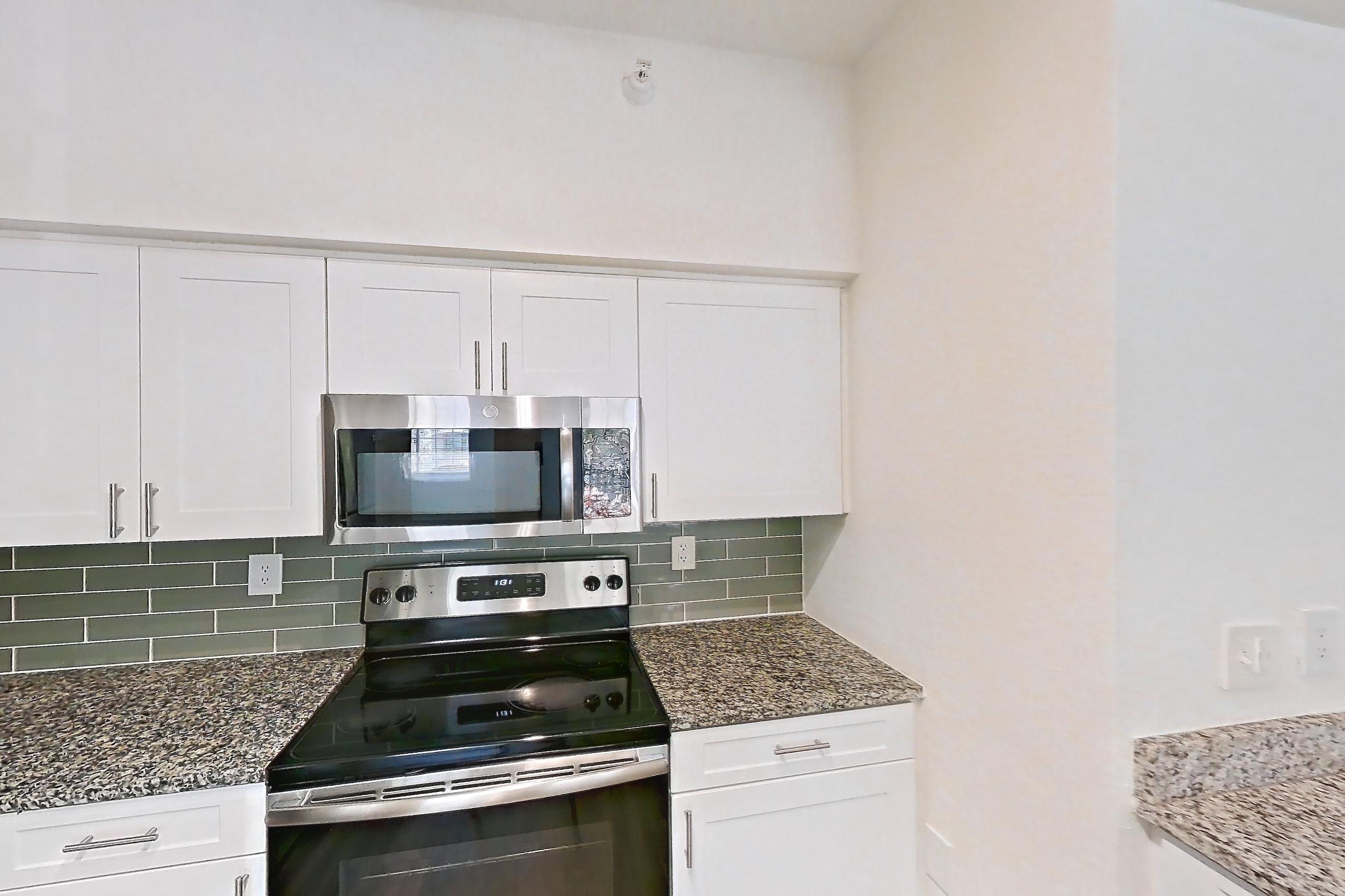 Kitchen with dark wood-finish flooring, dishwasher, electric range, light stone countertops, microwave, oven/range, refrigerator, and stainless steel appliances, Apartment 04-205 at Solano at Miramar
