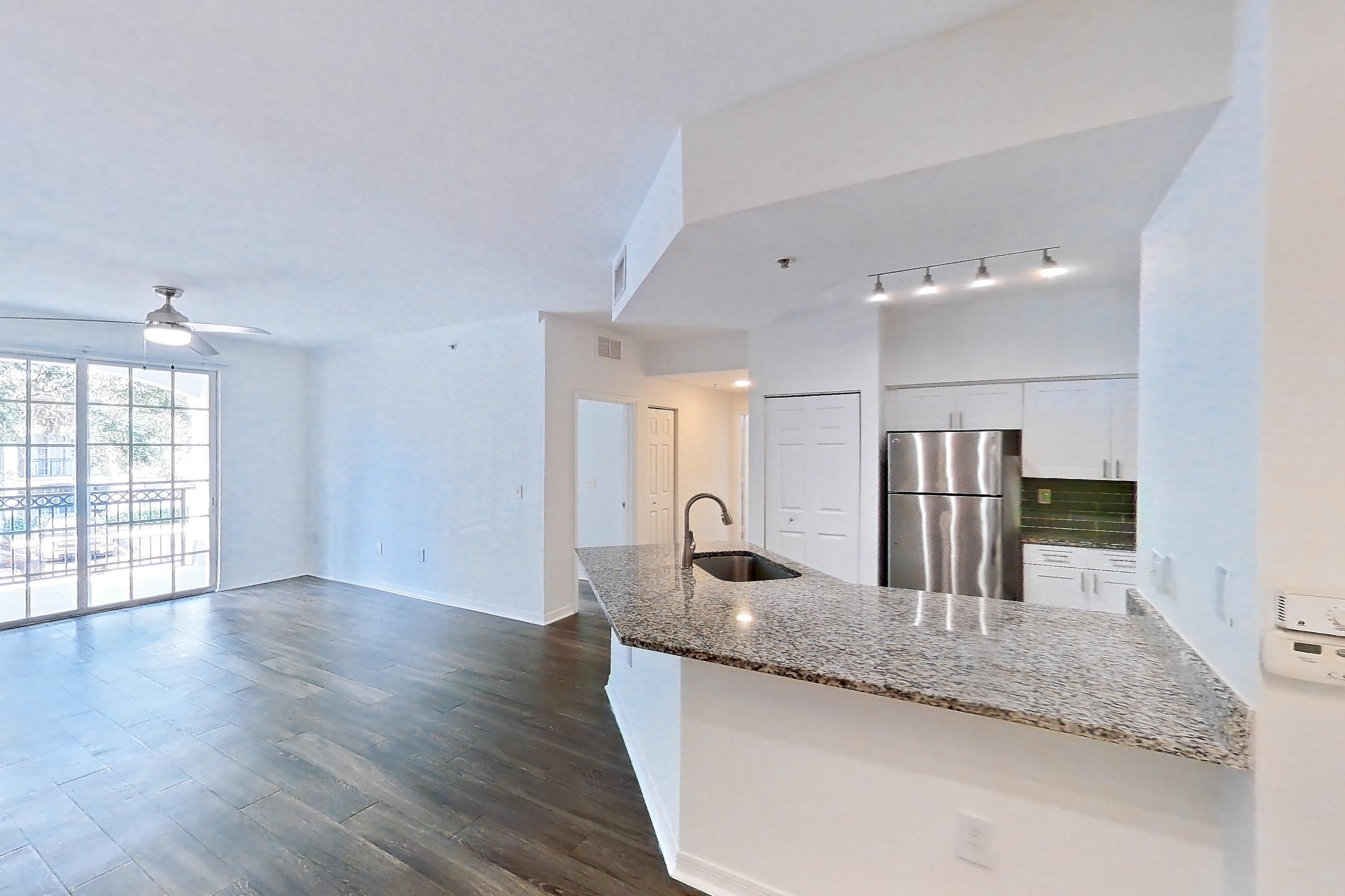 Living space with dark wood-finish flooring, light stone countertops, refrigerator, and stainless steel appliances, Apartment 04-205 at Solano at Miramar