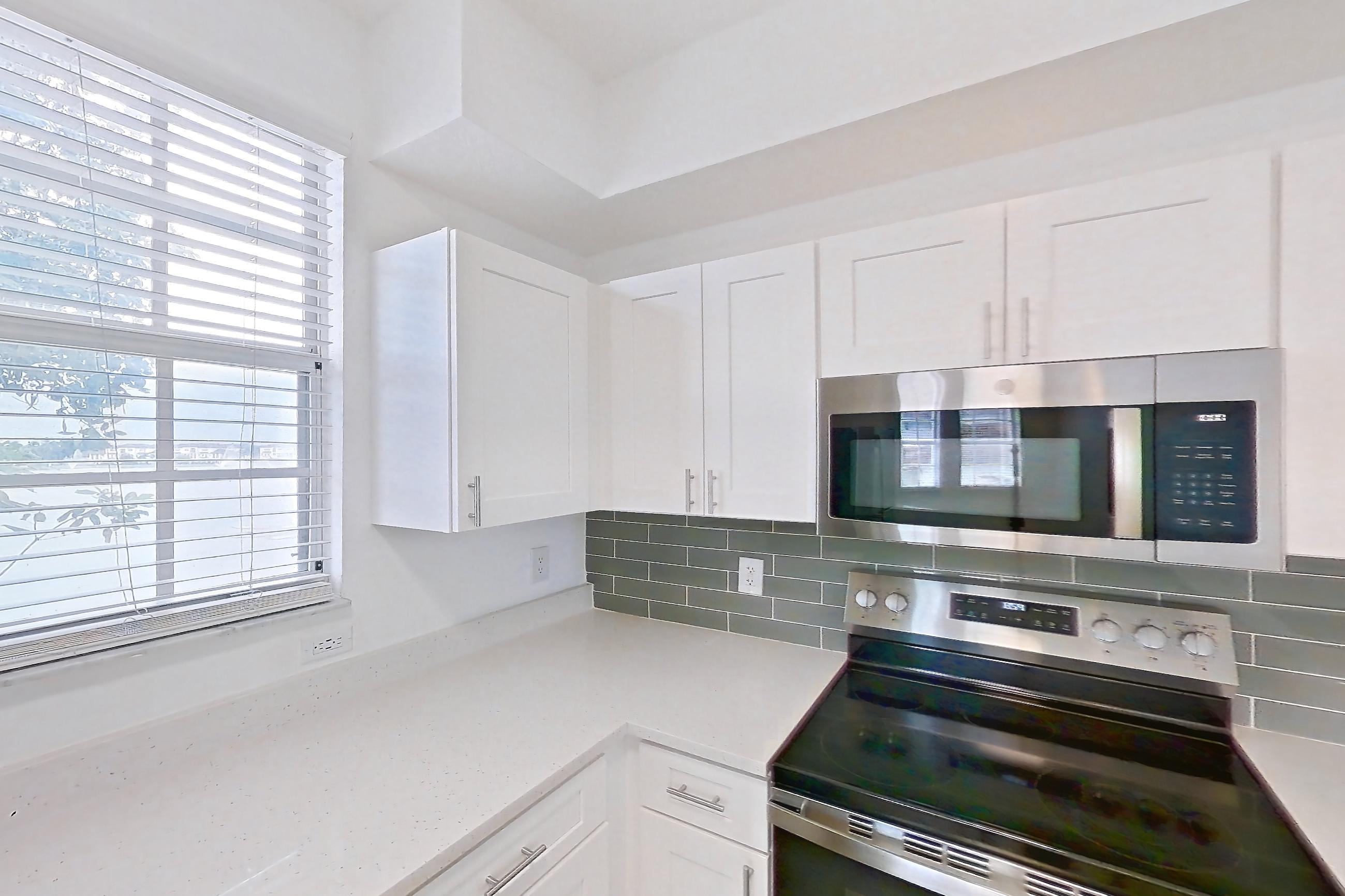 Kitchen with dishwasher, electric range, light countertops, light stone countertops, light wood-finish flooring, microwave, oven/range, refrigerator, and stainless steel appliances, Apartment 14-11734 at Solano at Miramar