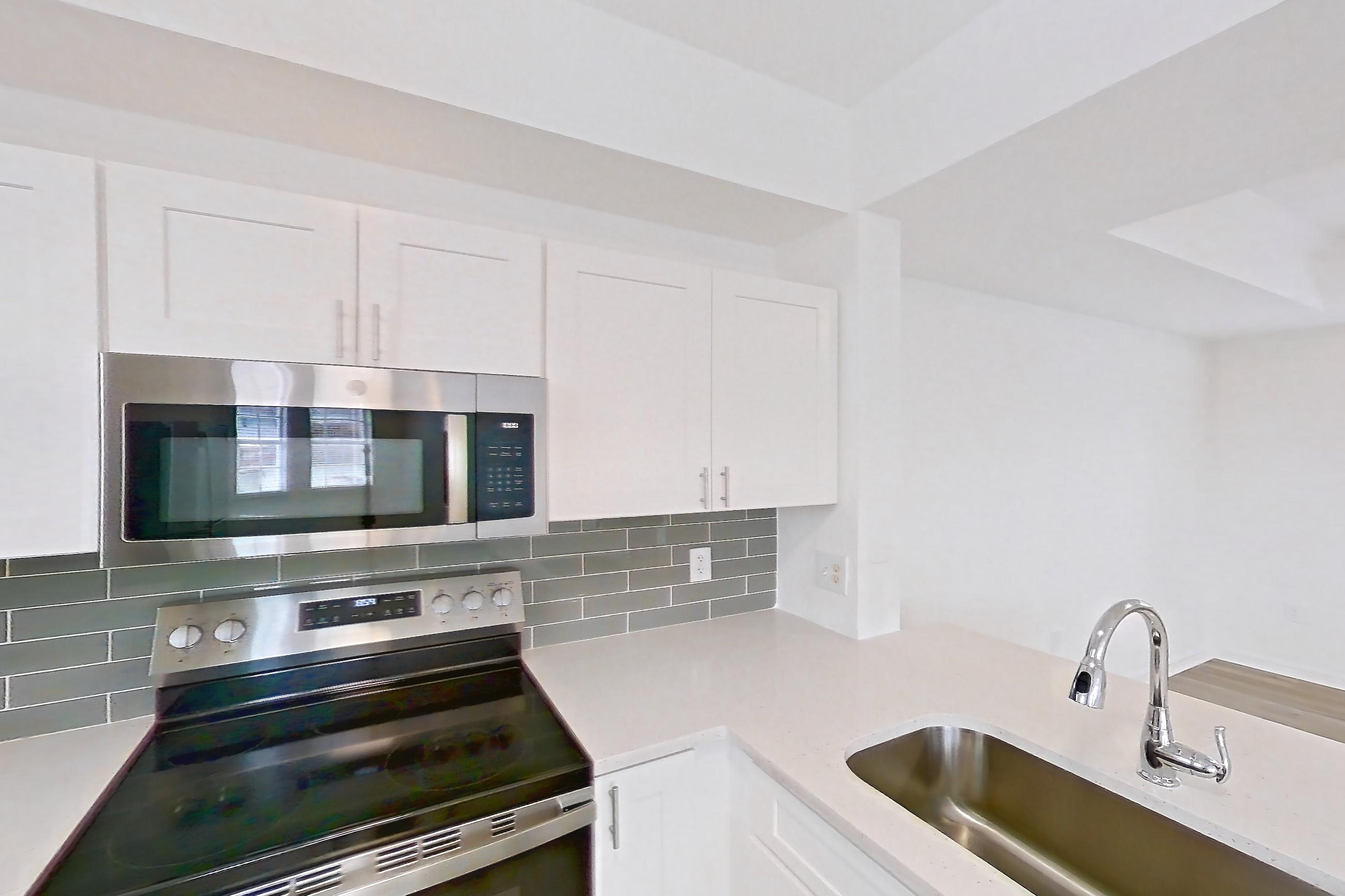 Kitchen with dishwasher, electric range, light countertops, light stone countertops, light wood-finish flooring, microwave, oven/range, refrigerator, and stainless steel appliances, Apartment 14-11734 at Solano at Miramar