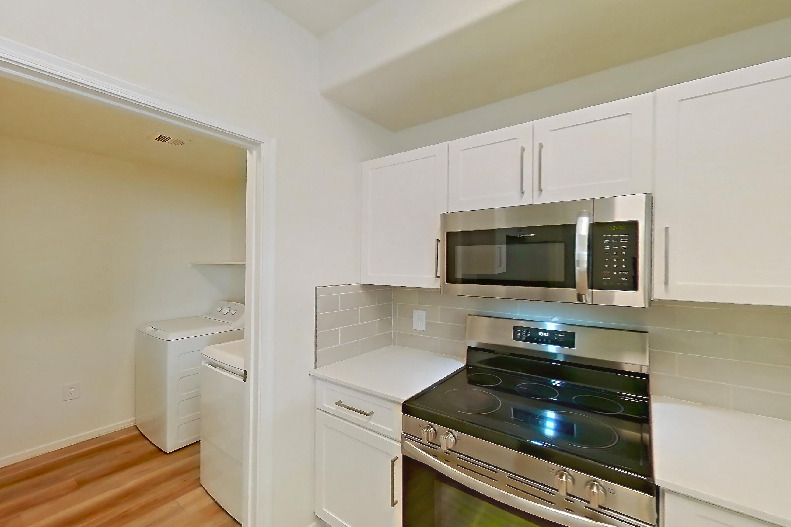 Kitchen with dishwasher, electric range, light countertops, light stone countertops, light wood-finish flooring, microwave, oven/range, and stainless steel appliances, Apartment 1033 at Dobson 2222