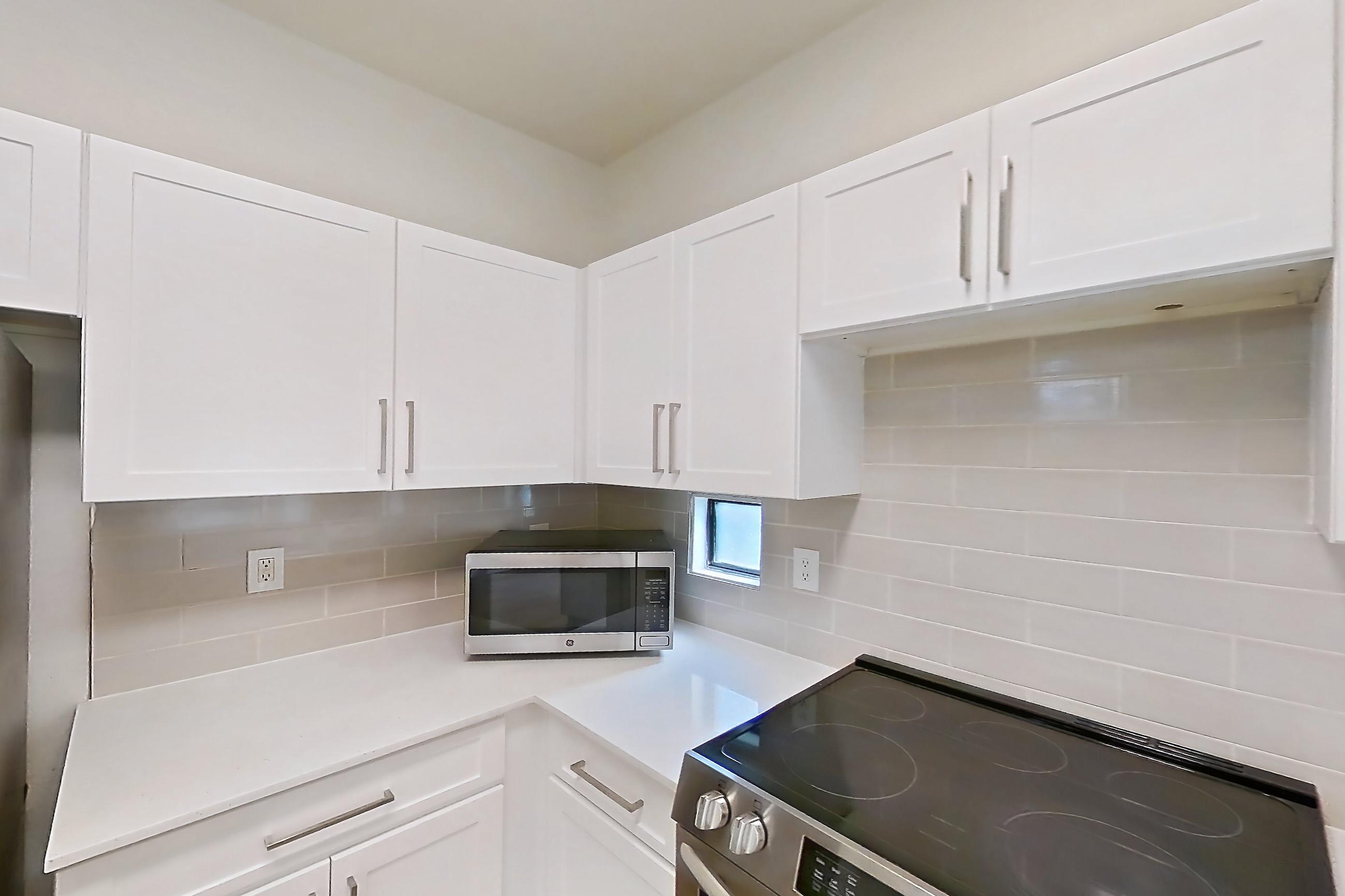 Kitchen with dishwasher, electric range, light countertops, light stone countertops, light wood-finish flooring, microwave, oven/range, and stainless steel appliances, Apartment 1087 at Dobson 2222