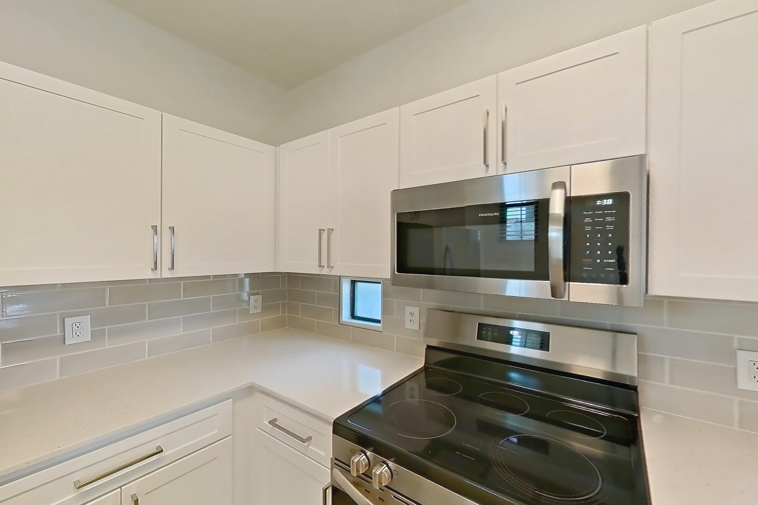 Kitchen with dishwasher, electric range, light countertops, light stone countertops, light wood-finish flooring, microwave, oven/range, and stainless steel appliances, Apartment 1091 at Dobson 2222