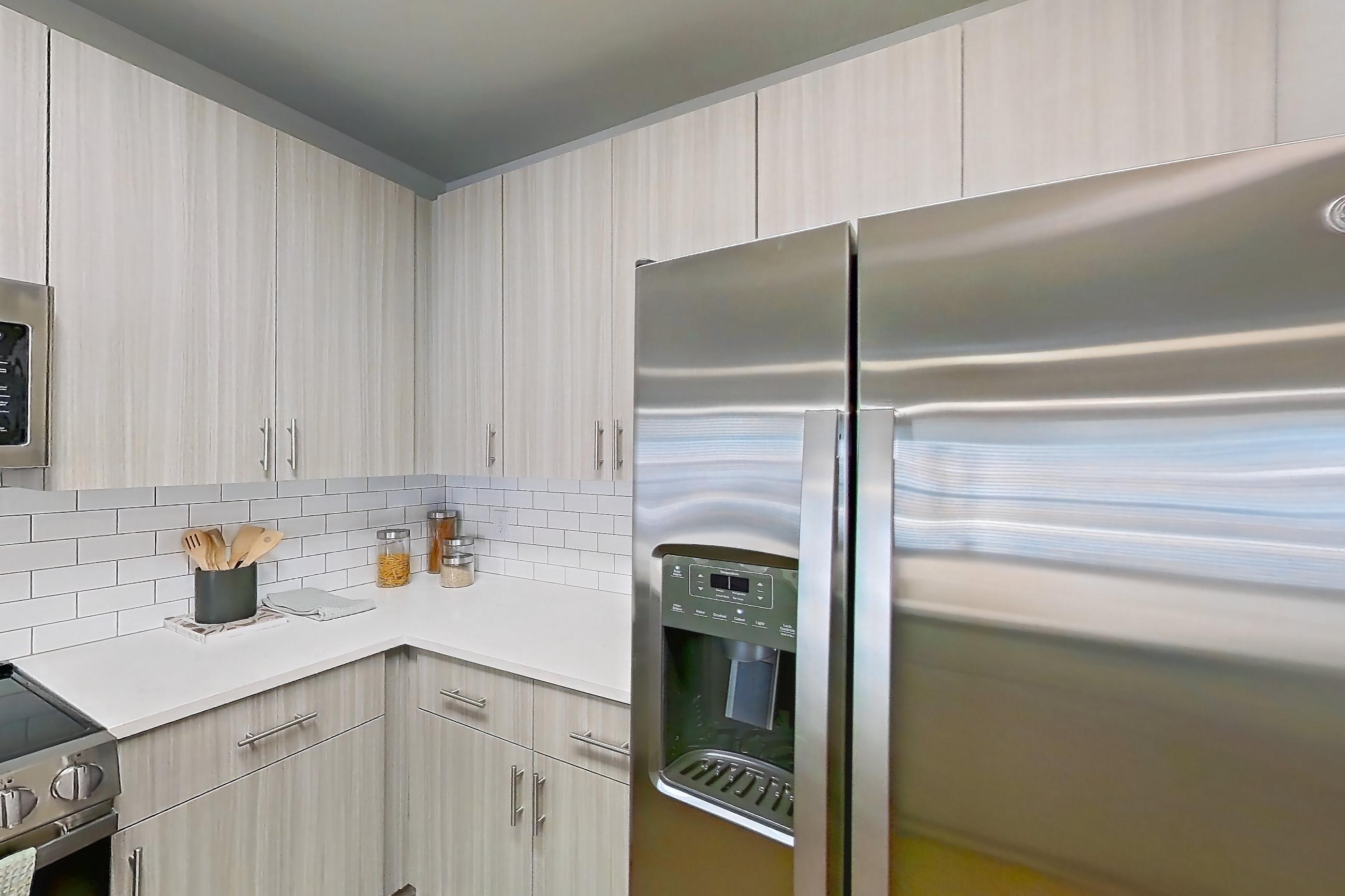 Kitchen with dark wood-finish flooring, dishwasher, electric range, kitchen island, light stone countertops, light wood-finish flooring, microwave, oven/range, refrigerator, stainless steel appliances, and water & ice dispenser, Apartment 4-201 at The Soho