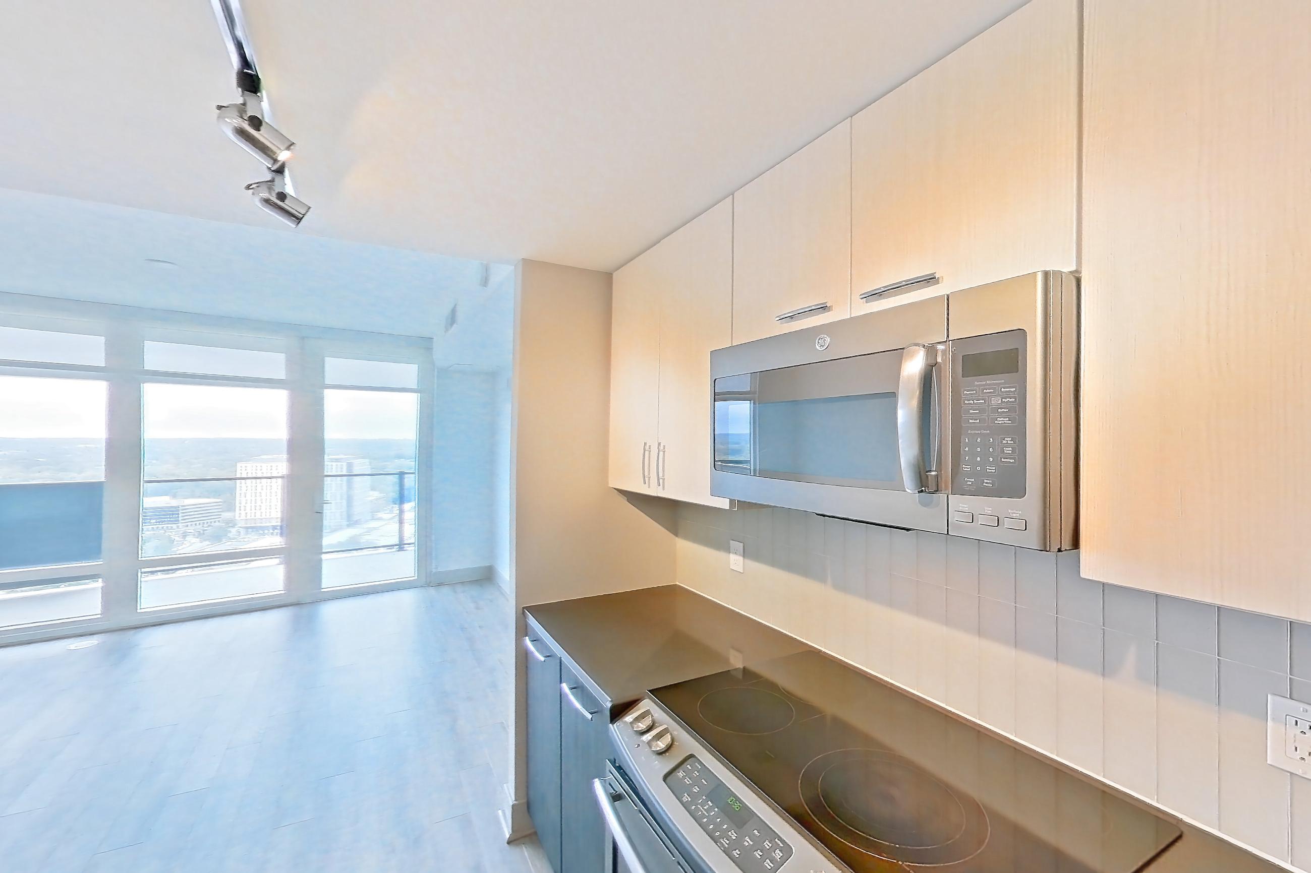 Kitchen with dark countertops, dark stone countertops, dishwasher, electric range, kitchen island, light wood-finish flooring, oven/range, and stainless steel appliances, Apartment 3013 at Adaire