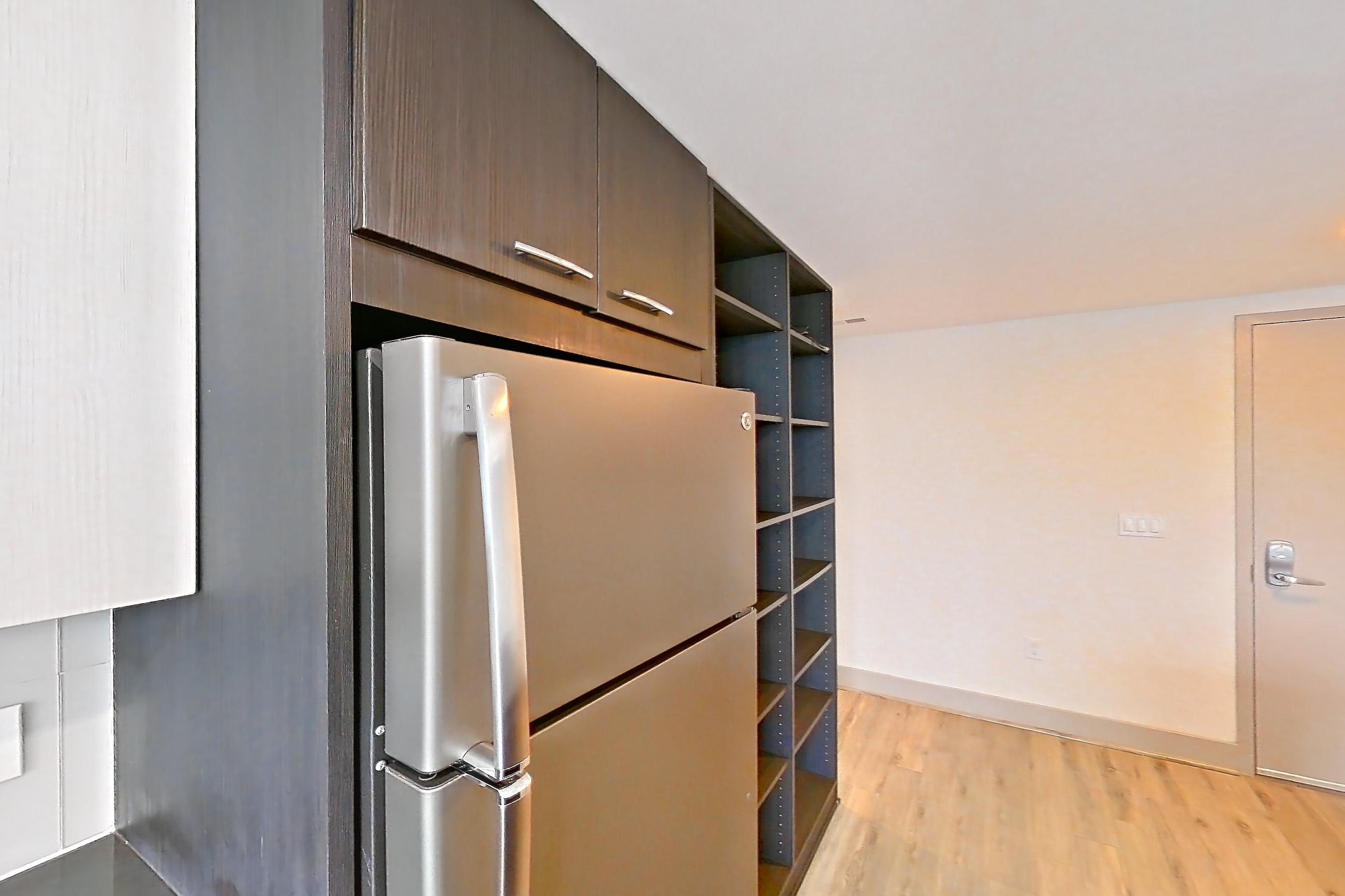 Kitchen with dark countertops, dark stone countertops, dishwasher, electric range, kitchen island, light wood-finish flooring, oven/range, refrigerator, and stainless steel appliances, Apartment 3113 at Adaire