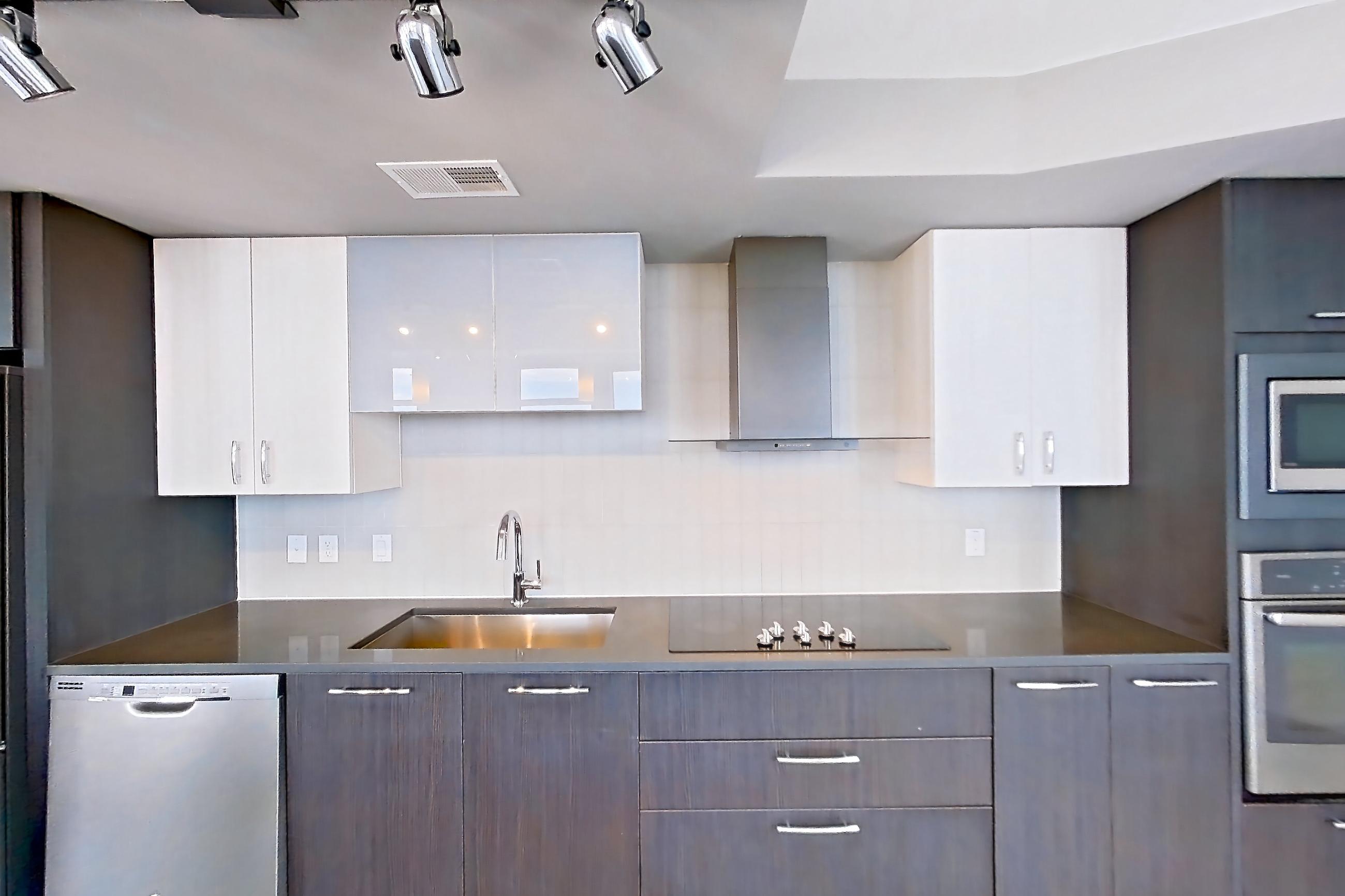 Kitchen with black appliances, cooktop, dark countertops, dishwasher, electric cooktop, light wood-finish flooring, refrigerator, stainless steel appliances, and white appliances, Apartment 2601 at Adaire