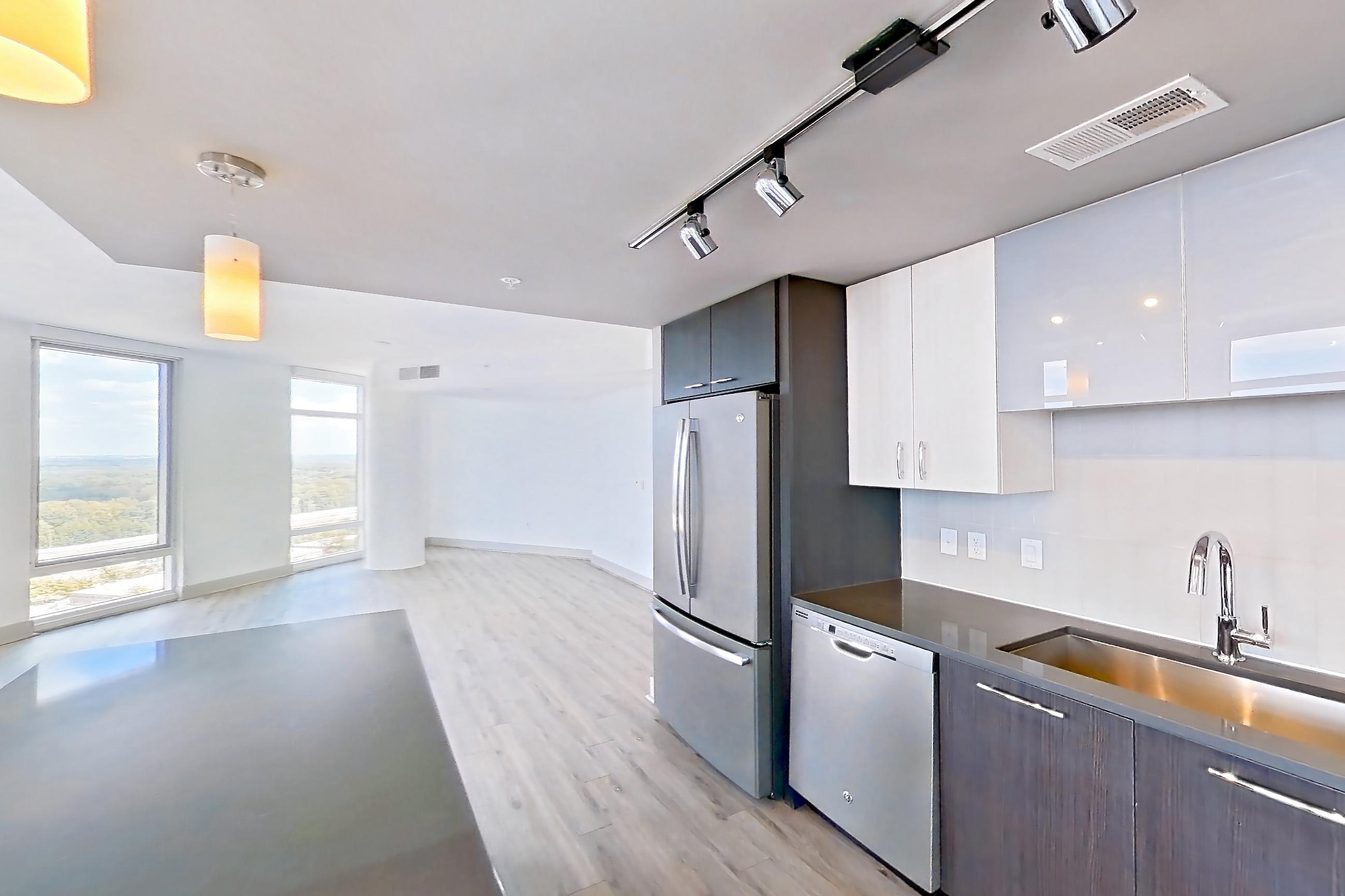 Kitchen with black appliances, cooktop, dark countertops, dishwasher, electric cooktop, light wood-finish flooring, refrigerator, stainless steel appliances, and white appliances, Apartment 2601 at Adaire