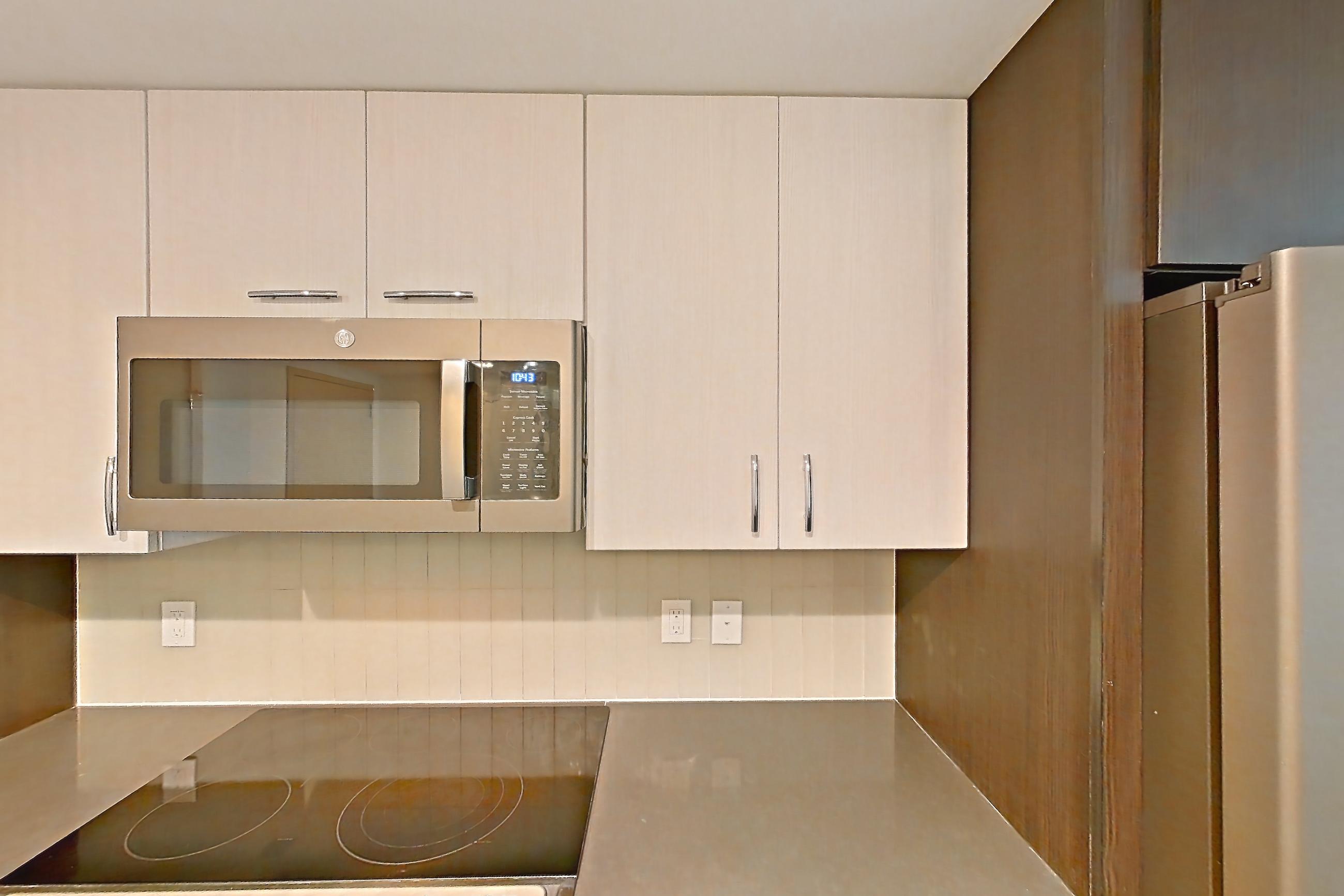 Kitchen with dark countertops, dishwasher, electric range, light countertops, light wood-finish flooring, microwave, oven/range, refrigerator, and stainless steel appliances, Apartment 3005 at Adaire