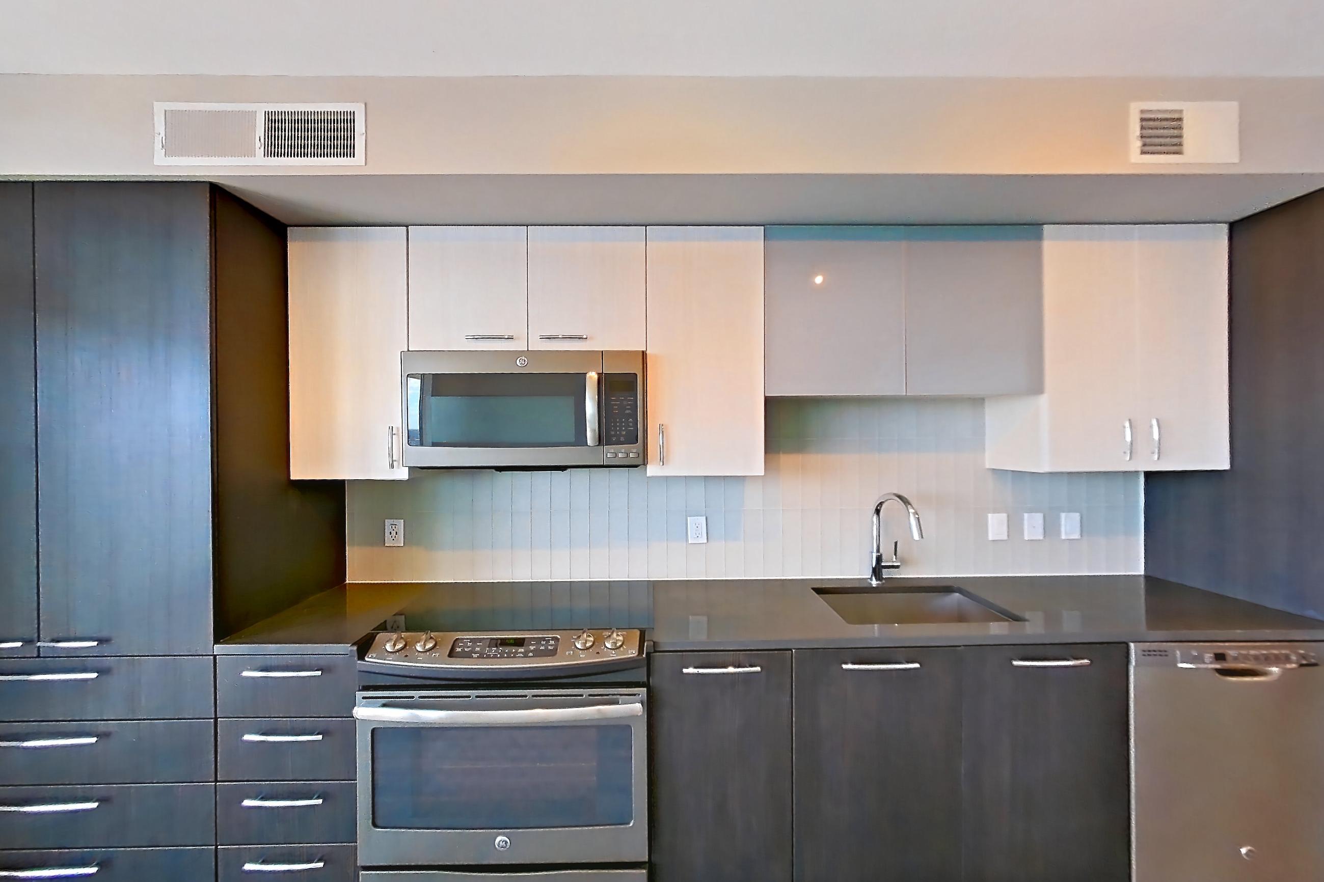 Kitchen with dark countertops, dishwasher, electric range, light wood-finish flooring, microwave, oven/range, refrigerator, and stainless steel appliances, Apartment 3215 at Adaire