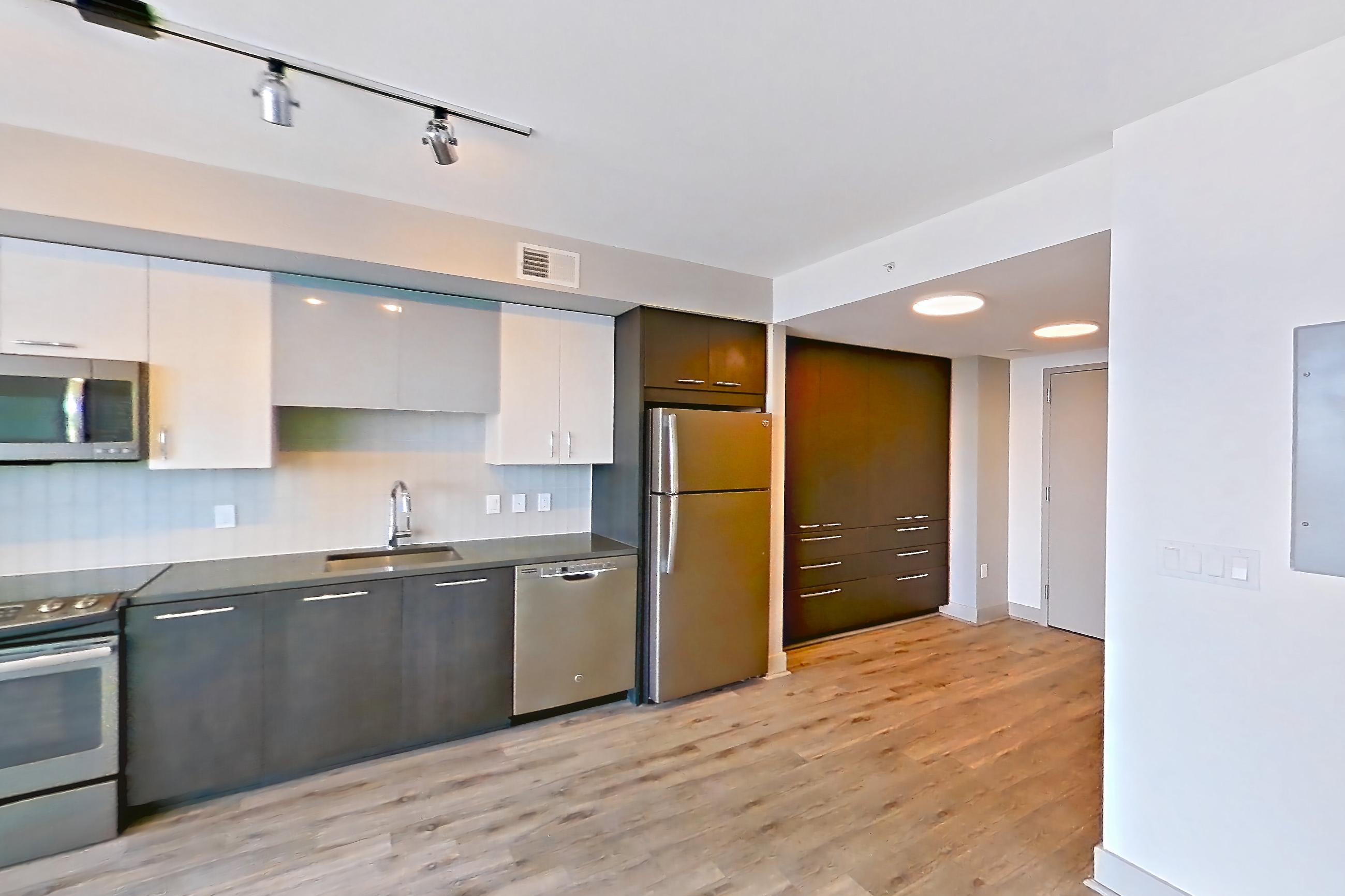 Living room with dark countertops, dishwasher, electric range, light countertops, light wood-finish flooring, microwave, oven/range, refrigerator, and stainless steel appliances, Apartment 3215 at Adaire