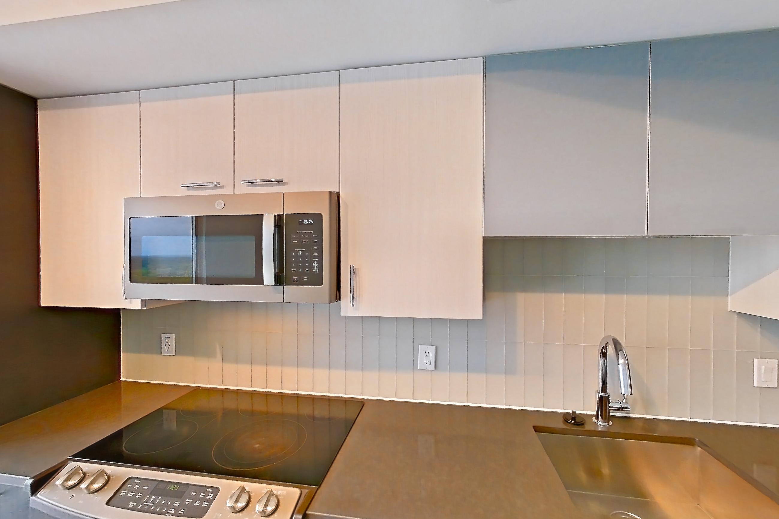 Kitchen with dark countertops, dishwasher, electric range, light countertops, light wood-finish flooring, microwave, oven/range, refrigerator, and stainless steel appliances, Apartment 1803 at Adaire