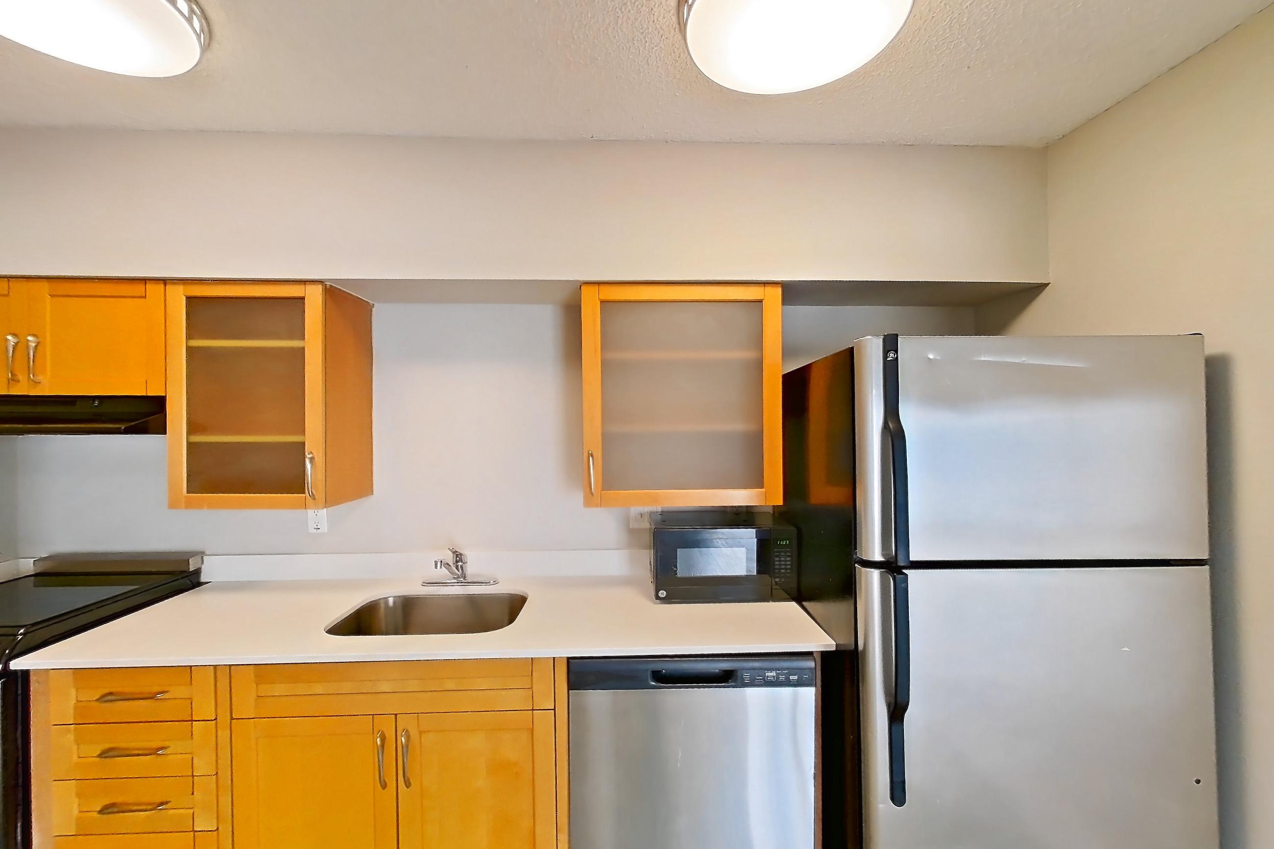 Kitchen with black appliances, dishwasher, light countertops, light wood-finish flooring, microwave, oven/range, refrigerator, and stainless steel appliances, Apartment 1012 at Pelican Lake
