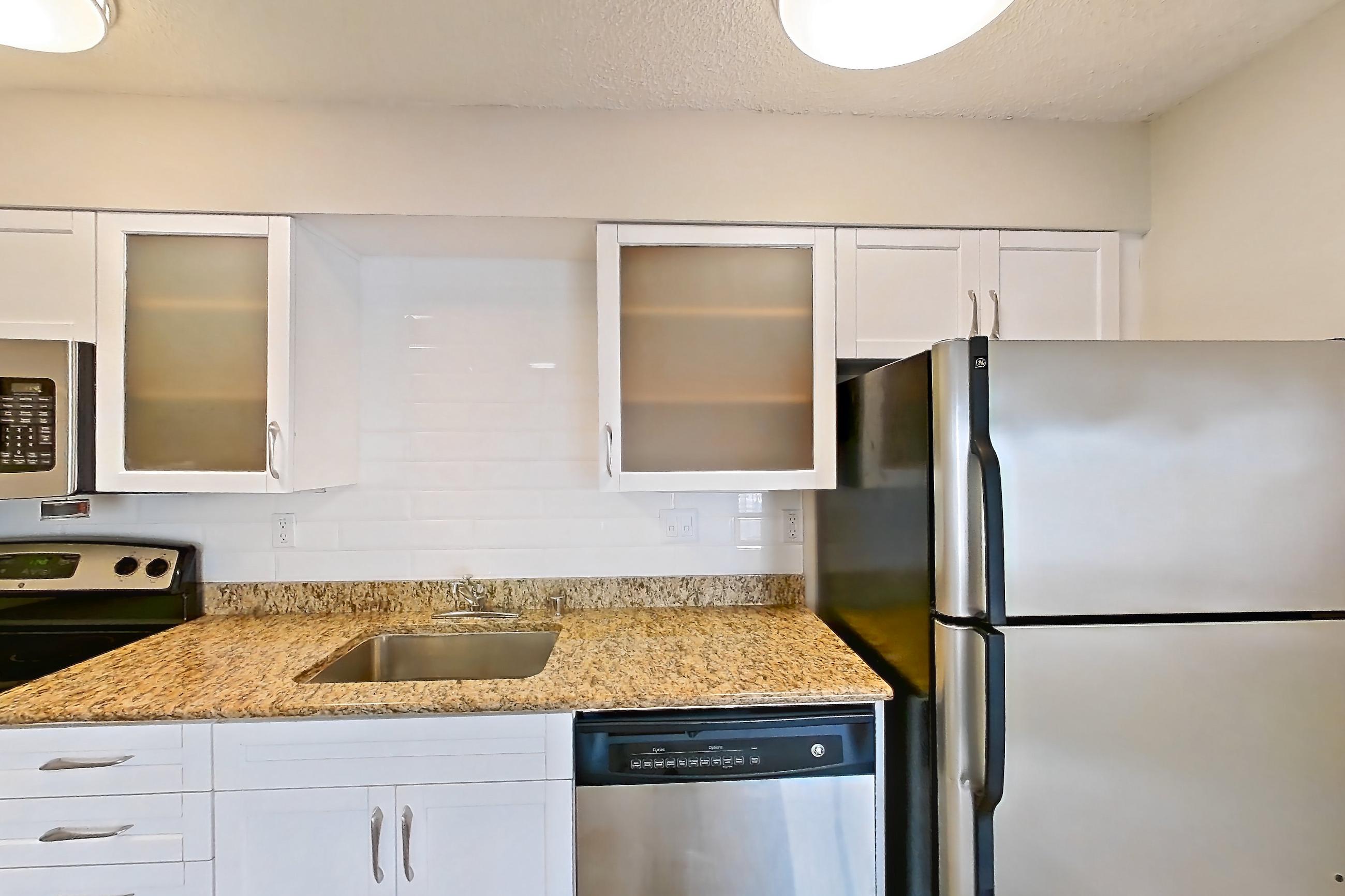 Kitchen with dishwasher, electric range, light countertops, light stone countertops, light wood-finish flooring, oven/range, refrigerator, and stainless steel appliances, Apartment 1022 at Pelican Lake