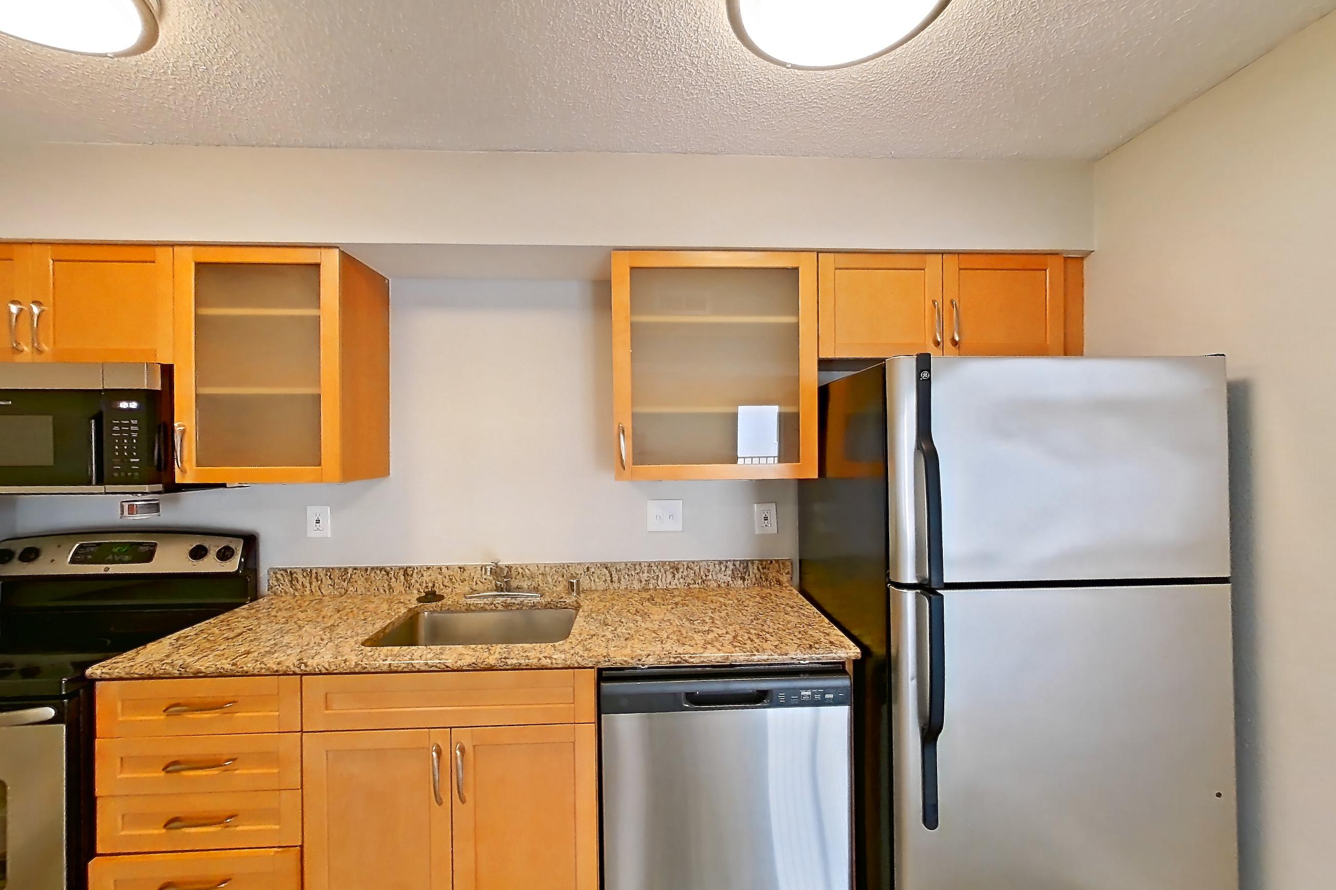 Kitchen with dishwasher, electric range, light stone countertops, light wood-finish flooring, oven/range, refrigerator, and stainless steel appliances, Apartment 522 at Pelican Lake