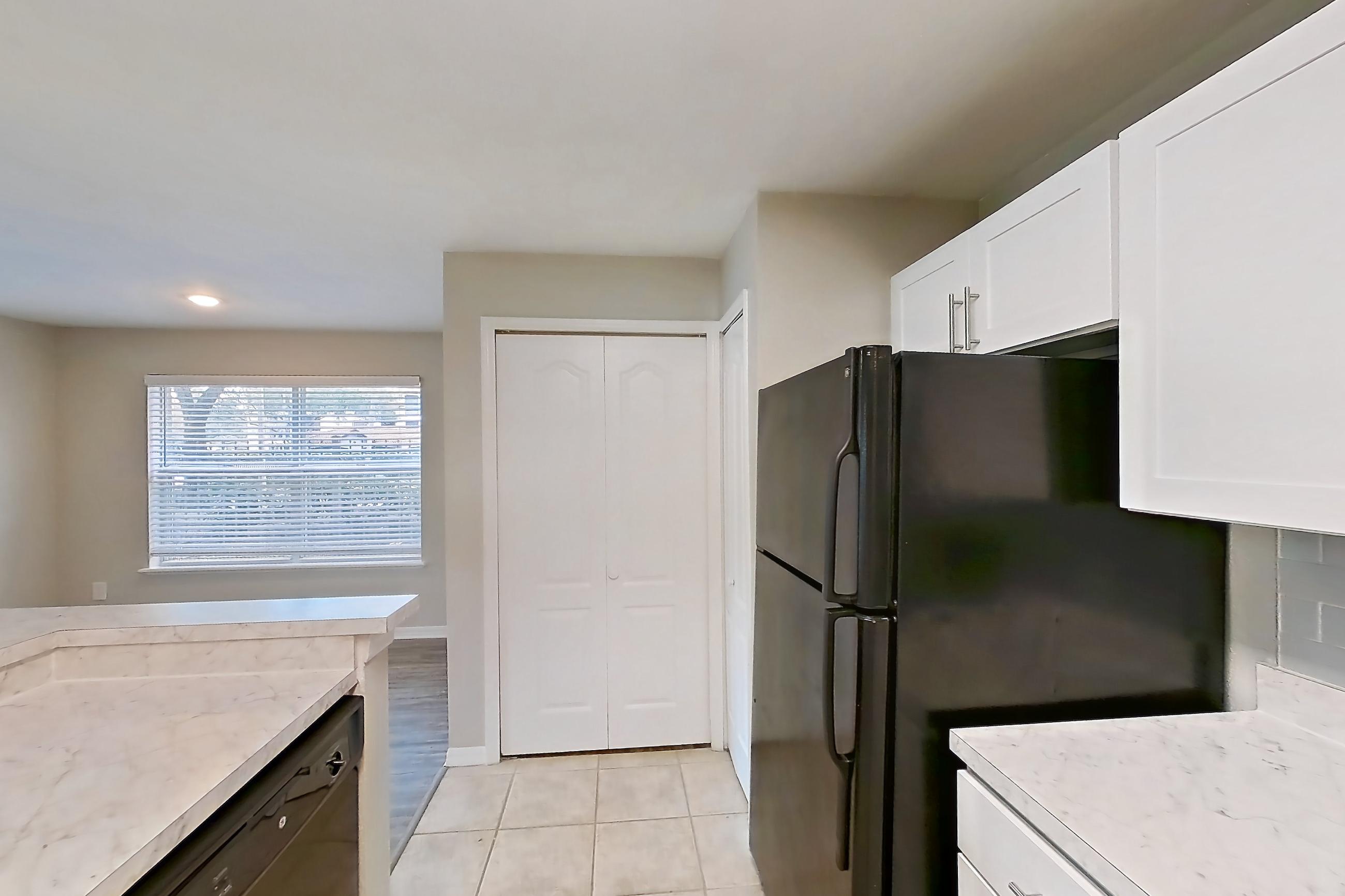 Kitchen with black appliances, dishwasher, electric range, kitchen island, light countertops, light tile flooring, microwave, oven/range, refrigerator, and stainless steel appliances, Apartment 01-102 at Boot Ranch