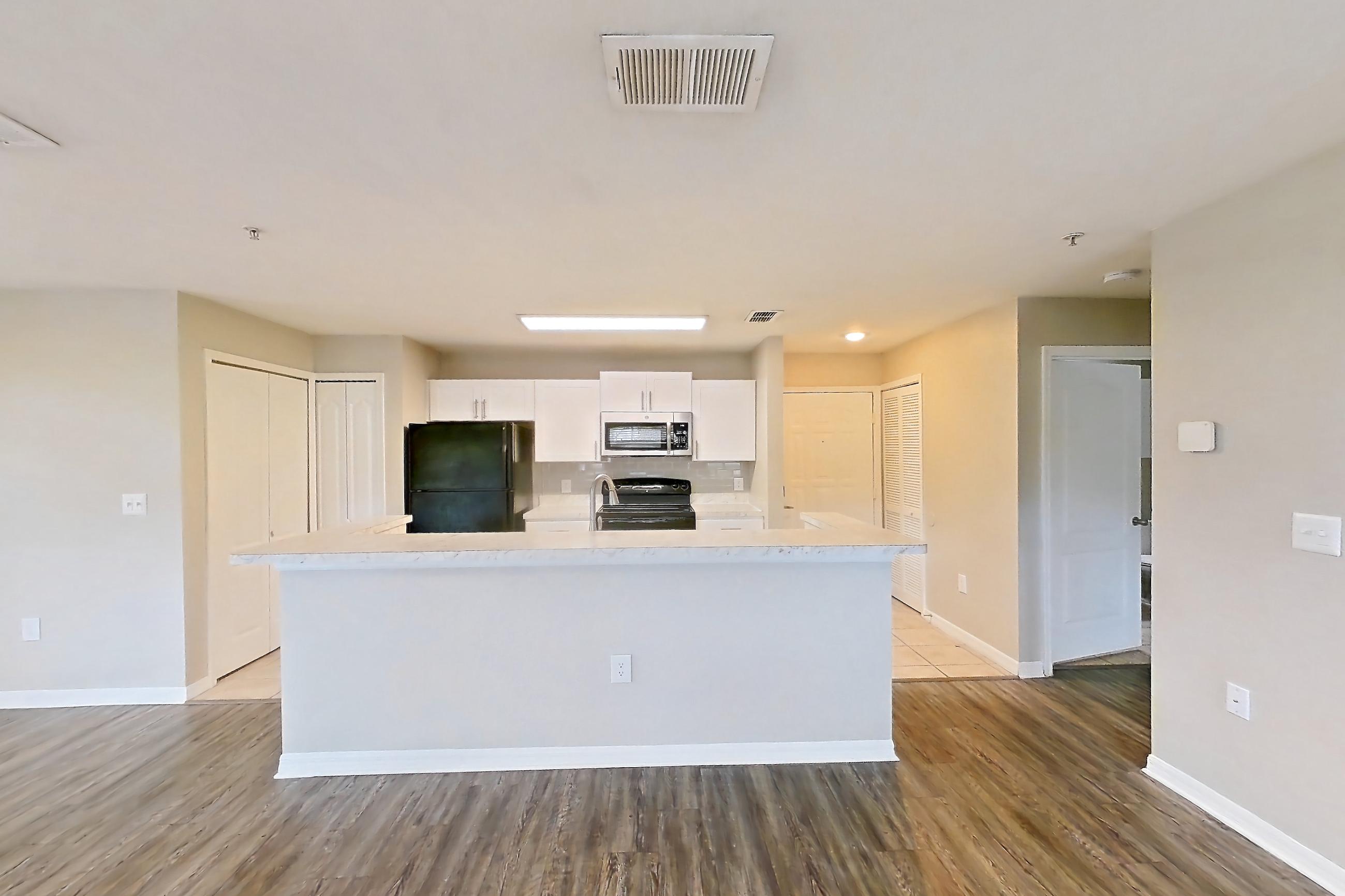 Living space with black appliances, dark wood-finish flooring, kitchen island, light countertops, light wood-finish flooring, oven/range, and refrigerator, Apartment 01-102 at Boot Ranch