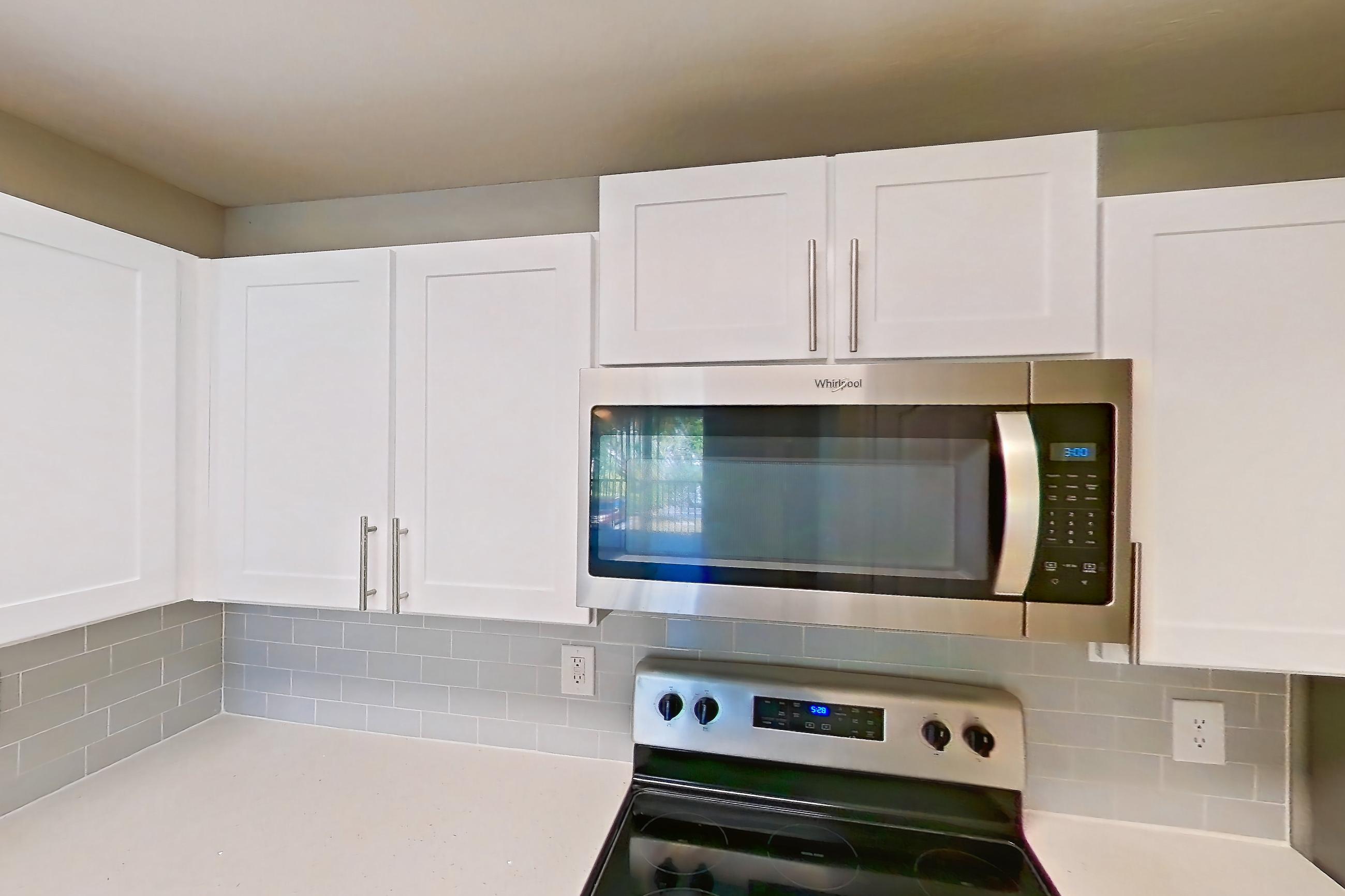 Kitchen with black appliances, dishwasher, electric range, light countertops, light stone countertops, light tile flooring, microwave, oven/range, refrigerator, and stainless steel appliances, Apartment 02-207 at Boot Ranch