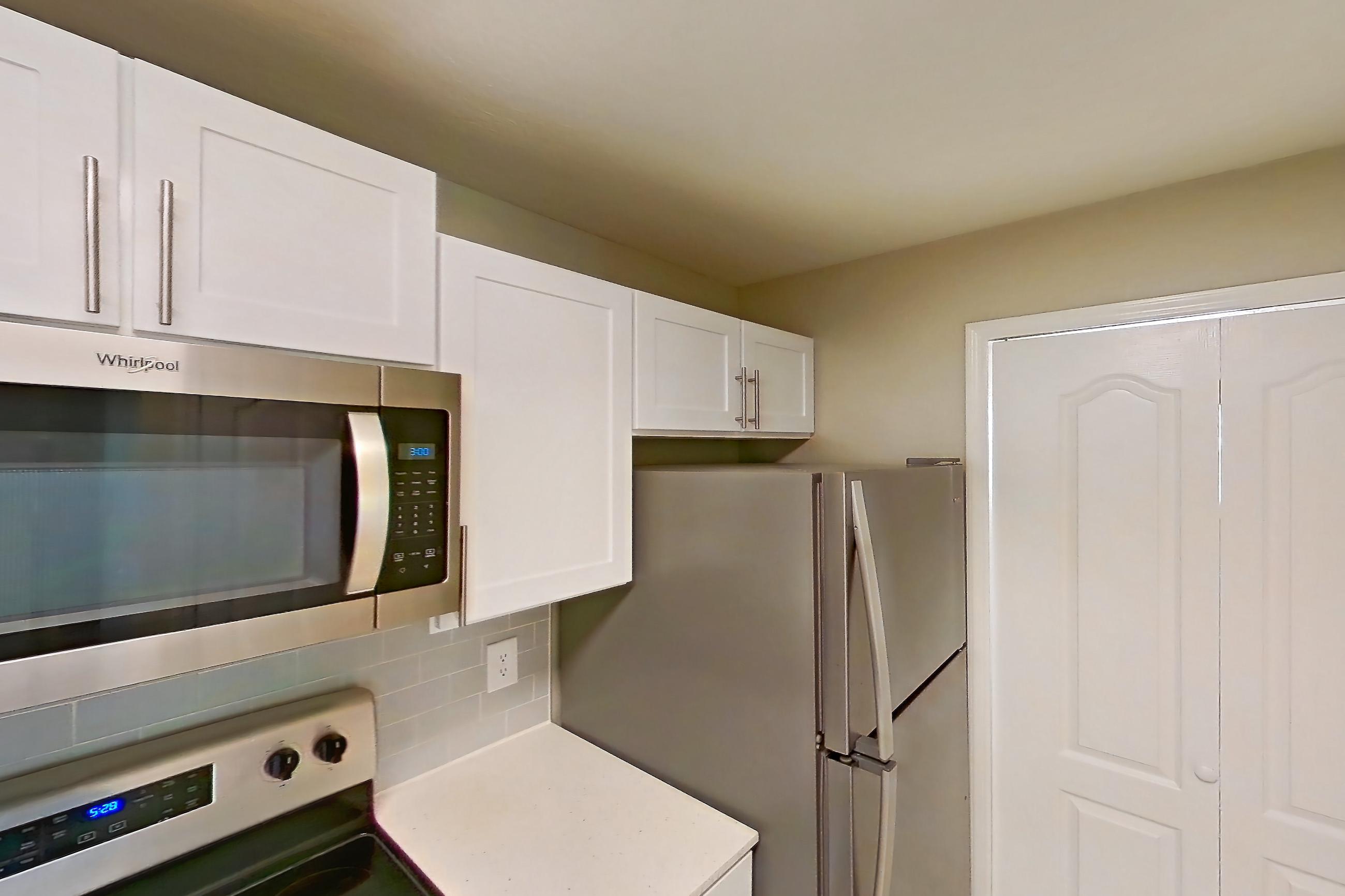 Kitchen with black appliances, dishwasher, electric range, light countertops, light stone countertops, light tile flooring, microwave, oven/range, refrigerator, and stainless steel appliances, Apartment 02-207 at Boot Ranch