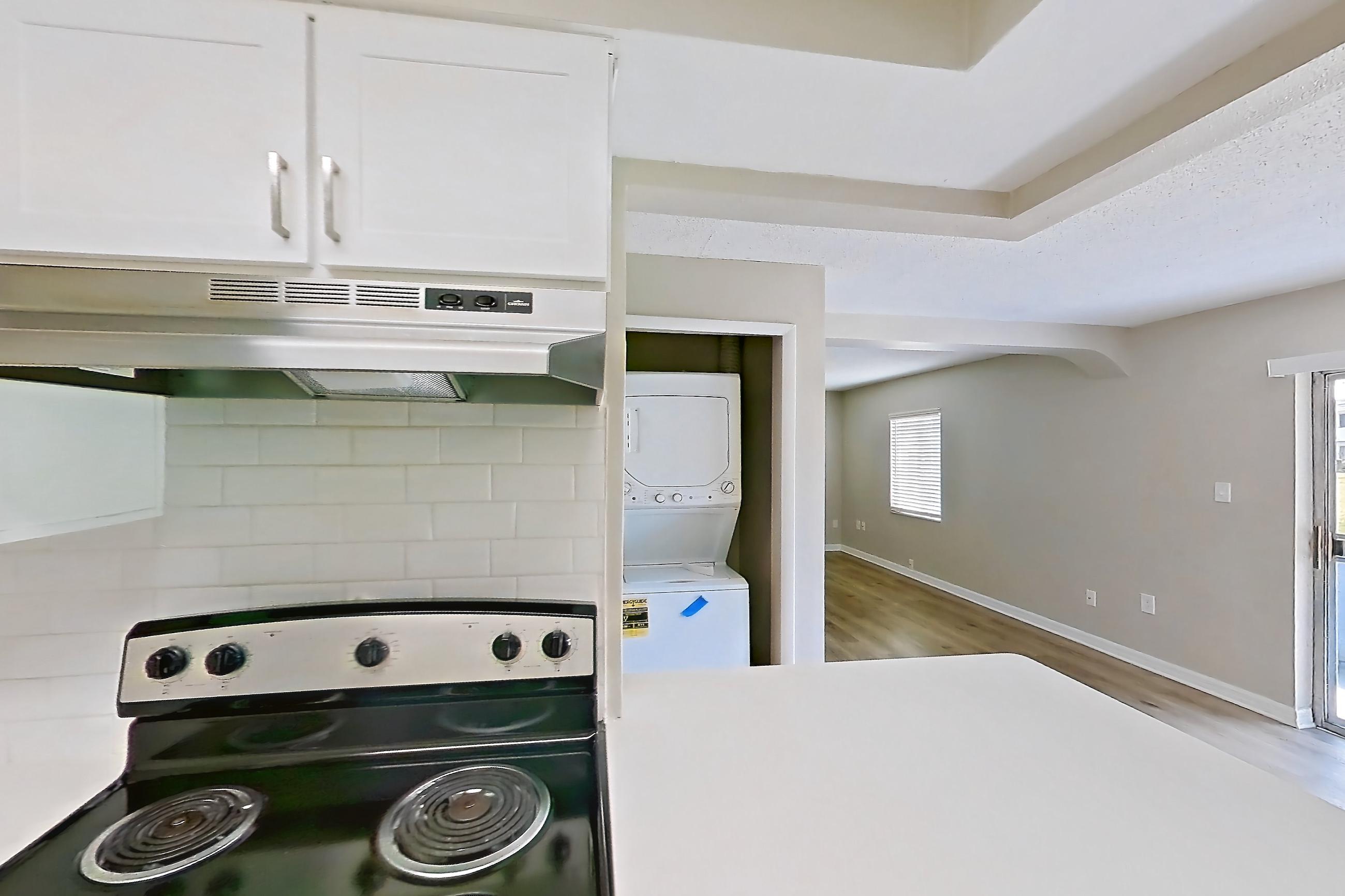 Kitchen with black appliances, electric range, in-unit laundry, light countertops, light wood-finish flooring, oven/range, range hood, refrigerator, and stainless steel appliances, Apartment 113 at Venue at Winter Park