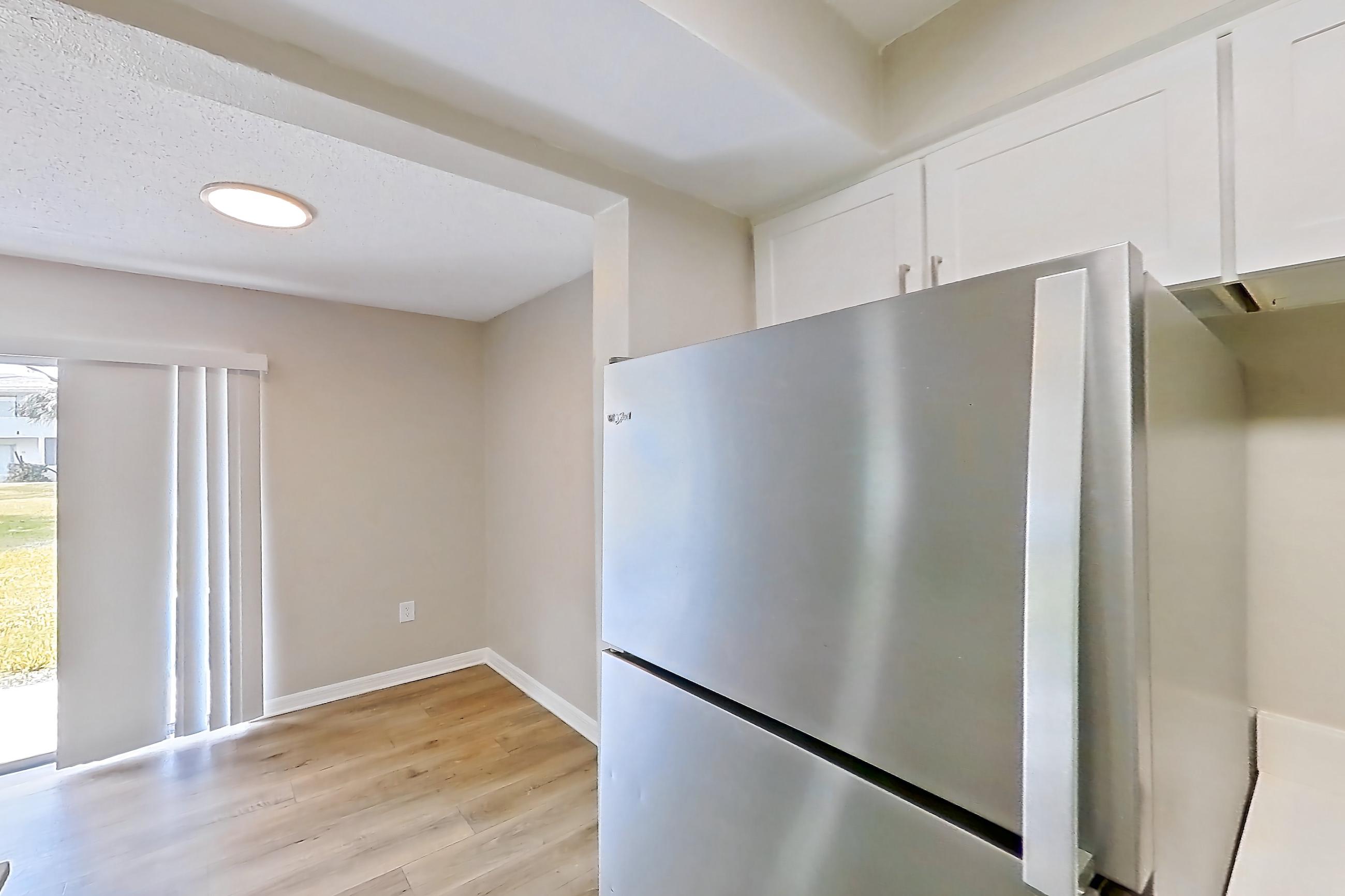 Kitchen with black appliances, electric range, in-unit laundry, light countertops, light wood-finish flooring, oven/range, range hood, refrigerator, and stainless steel appliances, Apartment 113 at Venue at Winter Park