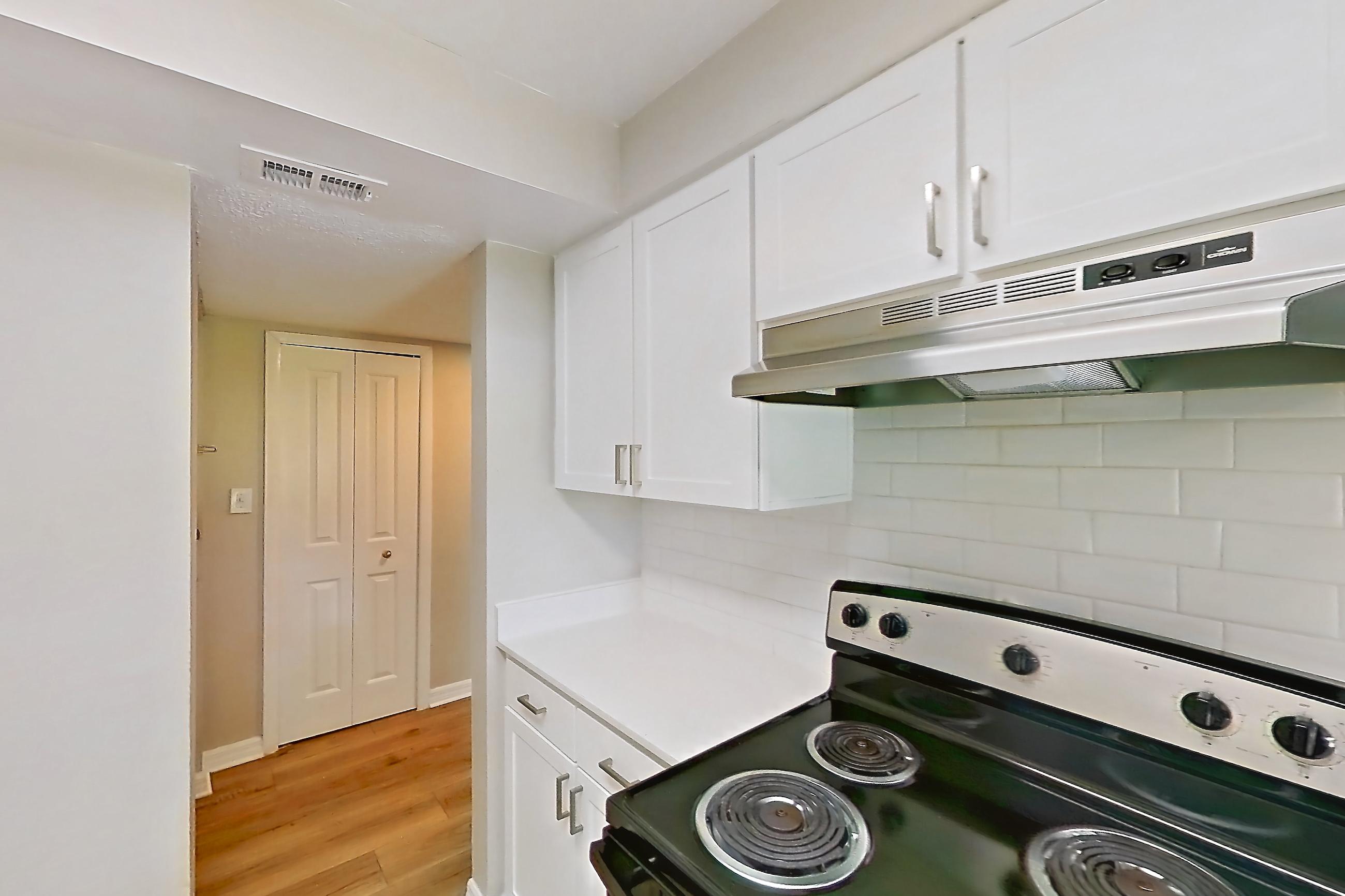 Kitchen with black appliances, electric range, in-unit laundry, light countertops, light wood-finish flooring, oven/range, range hood, refrigerator, and stainless steel appliances, Apartment 113 at Venue at Winter Park