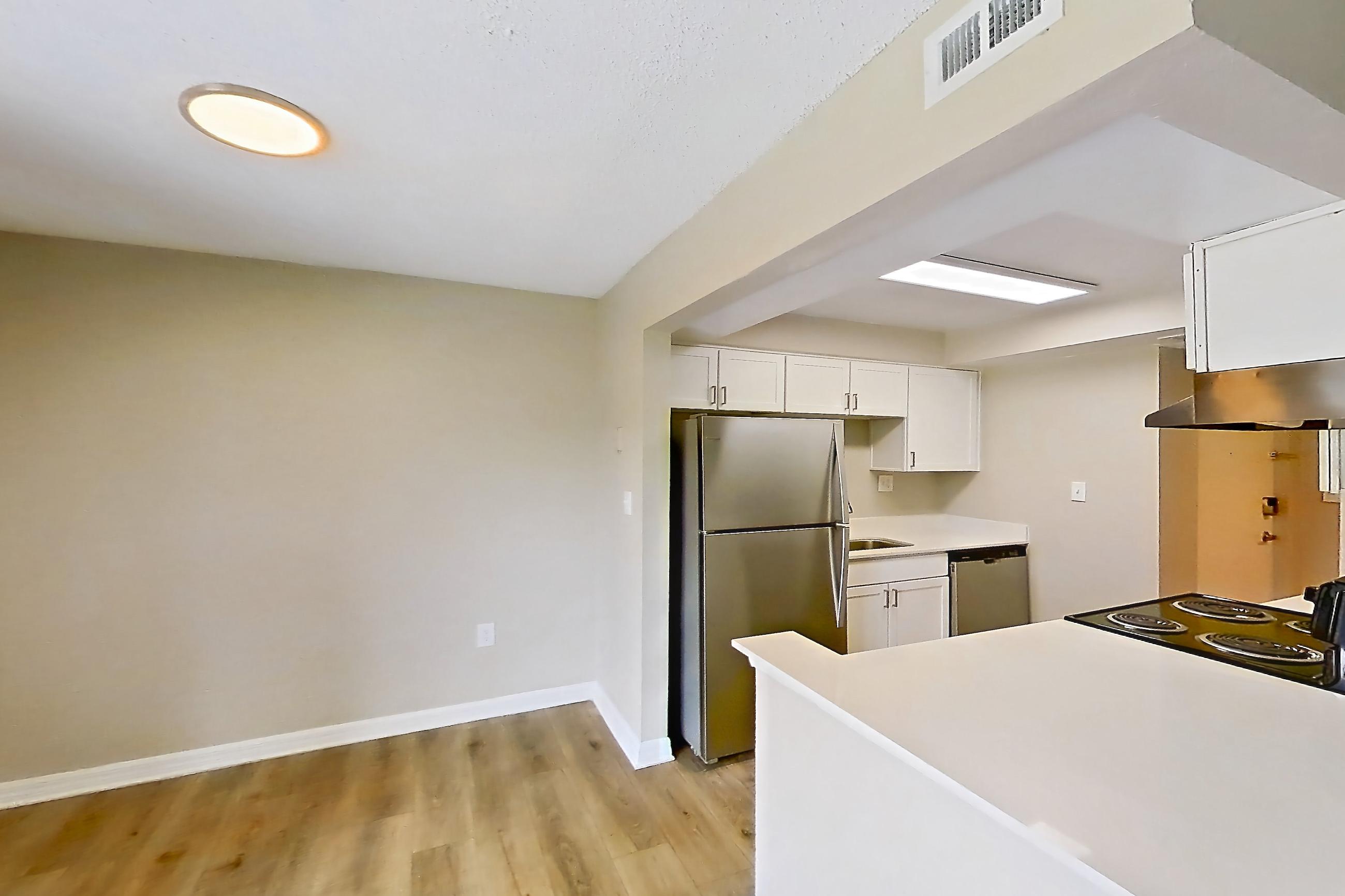 Living space with black appliances, dishwasher, electric range, in-unit laundry, light countertops, light wood-finish flooring, oven/range, refrigerator, and stainless steel appliances, Apartment 113 at Venue at Winter Park