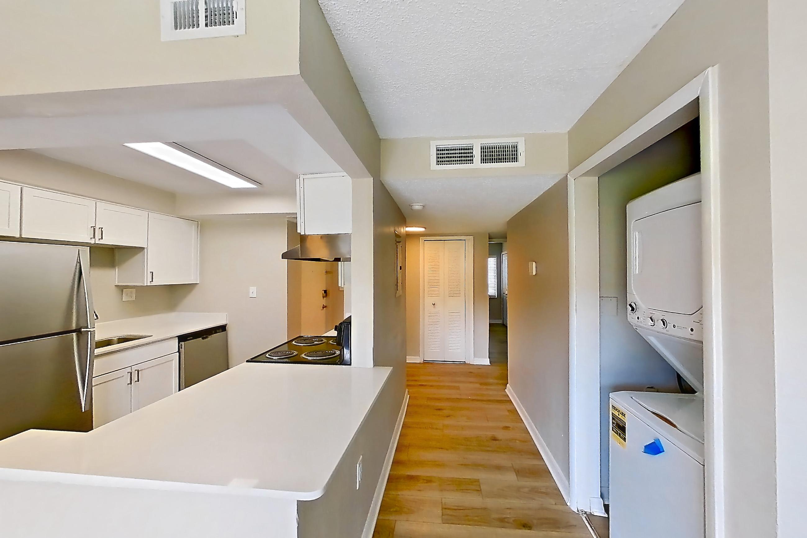 Living space with black appliances, dishwasher, electric range, in-unit laundry, light countertops, light wood-finish flooring, oven/range, refrigerator, and stainless steel appliances, Apartment 113 at Venue at Winter Park