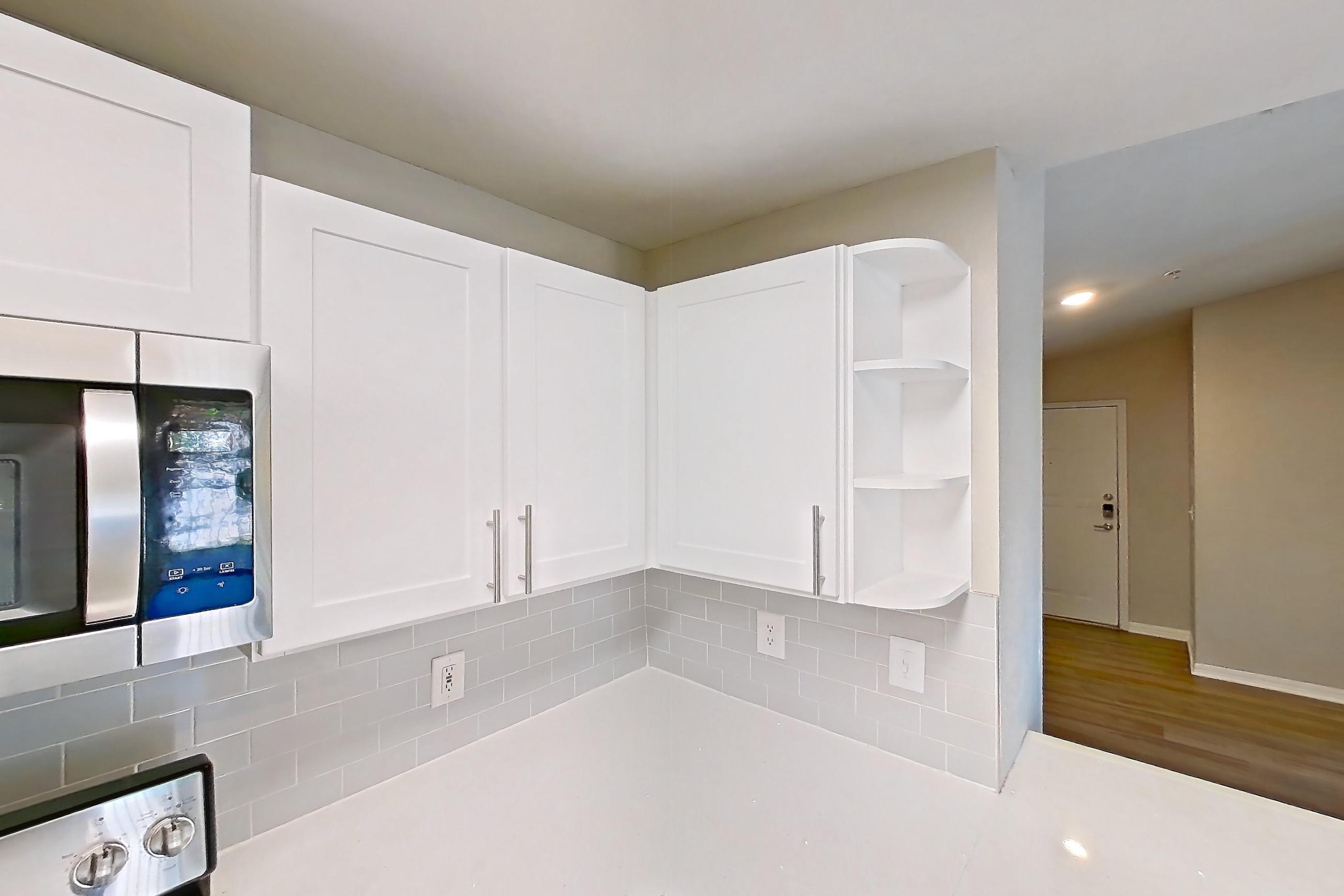 Kitchen with dark wood-finish flooring, dishwasher, electric range, light countertops, light stone countertops, light wood-finish flooring, microwave, oven/range, refrigerator, and stainless steel appliances, Apartment 02-301 at Boot Ranch
