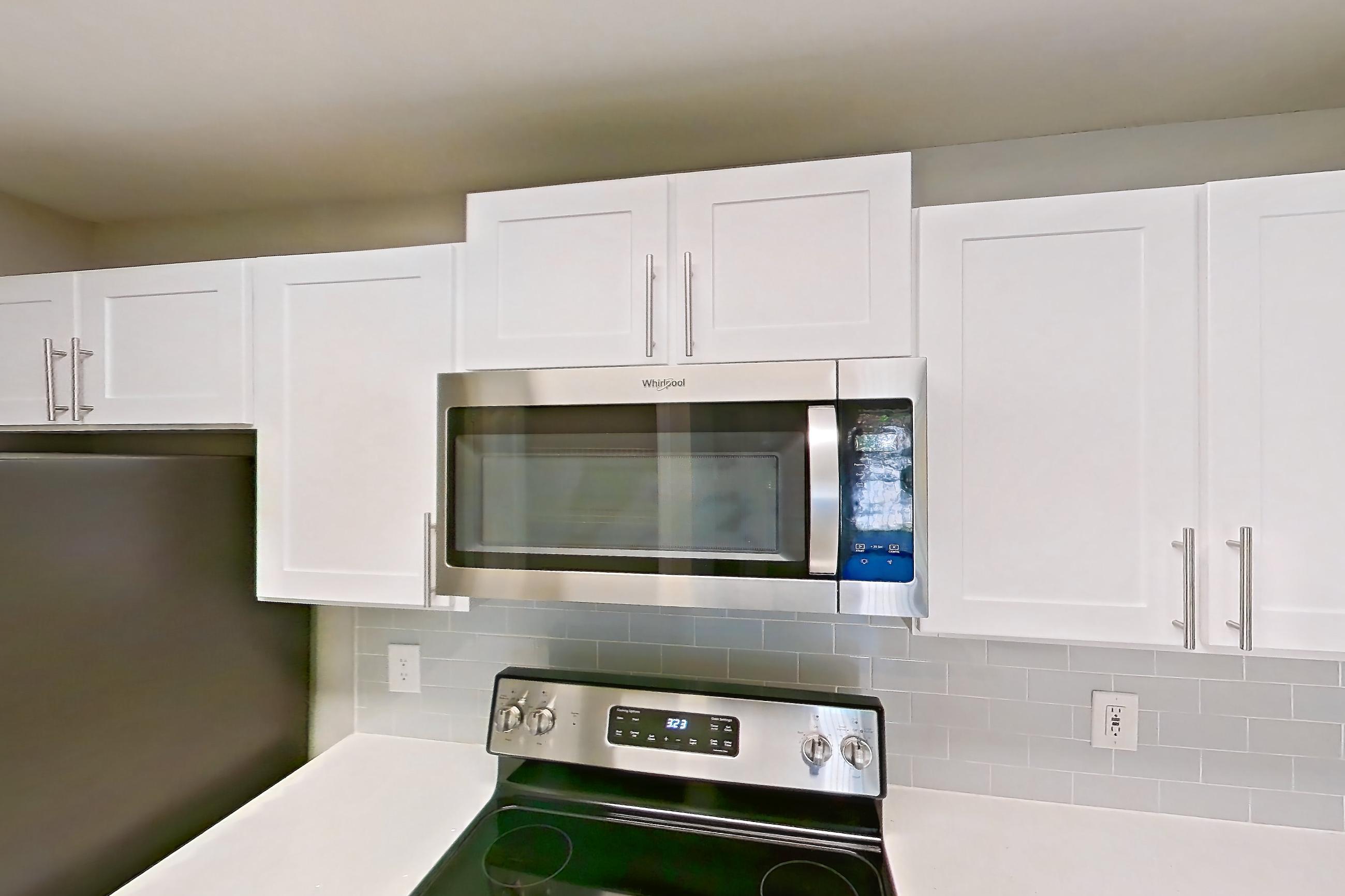 Kitchen with dark wood-finish flooring, dishwasher, electric range, light countertops, light stone countertops, light wood-finish flooring, microwave, oven/range, refrigerator, and stainless steel appliances, Apartment 02-301 at Boot Ranch