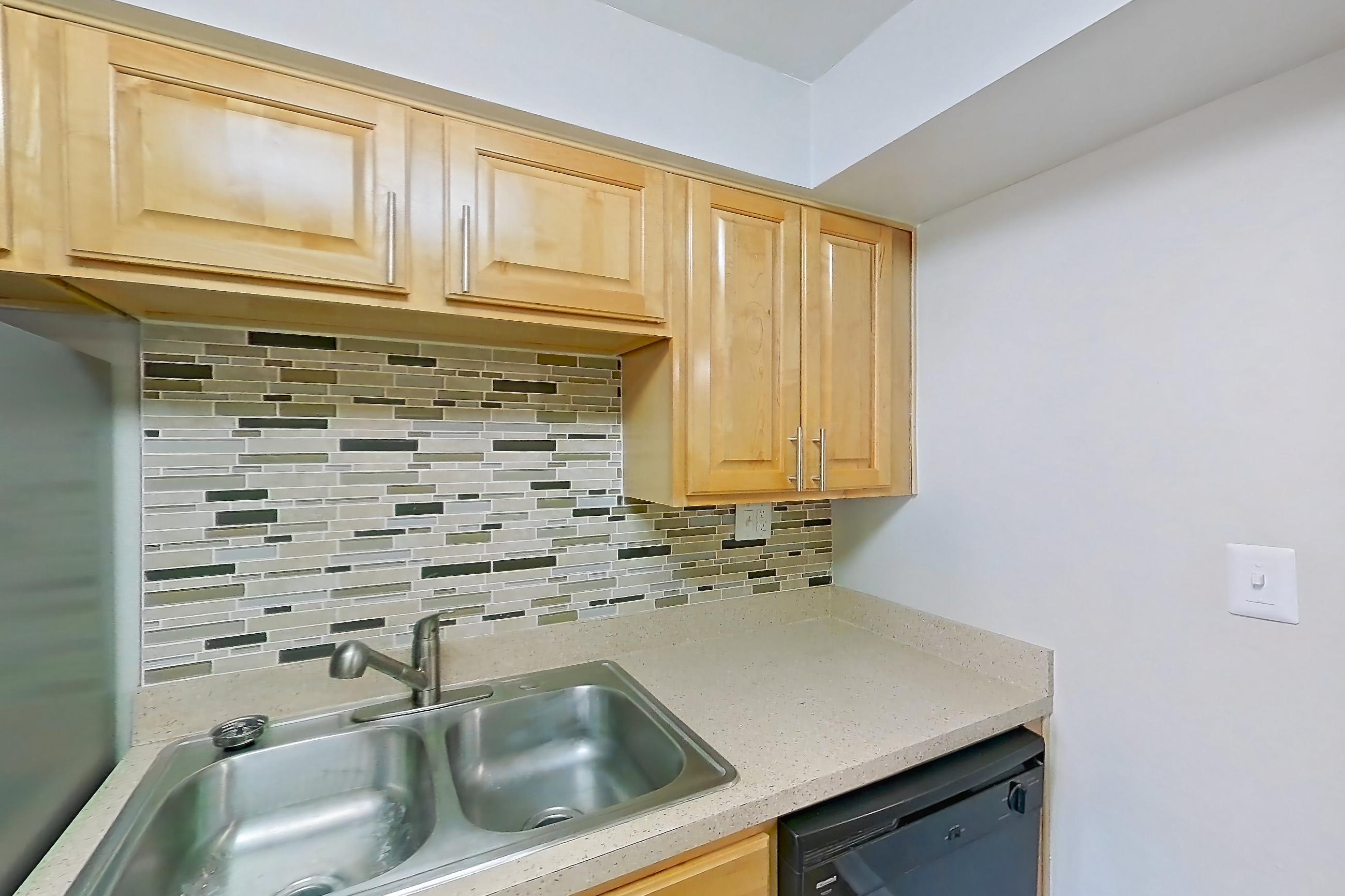 Kitchen with black appliances, dark wood-finish flooring, dishwasher, electric range, light countertops, light stone countertops, oven/range, range hood, refrigerator, stainless steel appliances, and white appliances, Apartment 121 at Venue at Winter Park