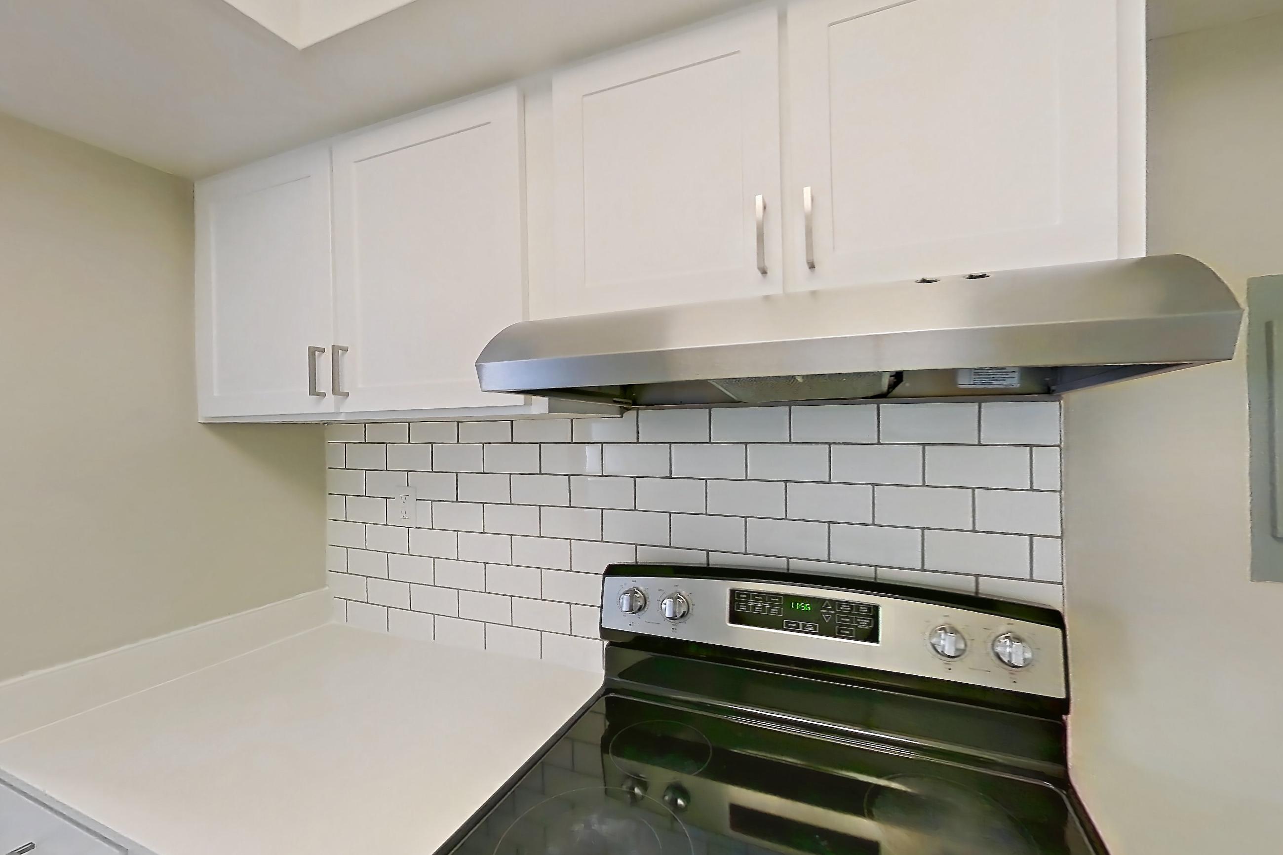 Kitchen with dishwasher, electric range, light countertops, light wood-finish flooring, oven/range, range hood, refrigerator, and stainless steel appliances, Apartment 172 at Venue at Winter Park