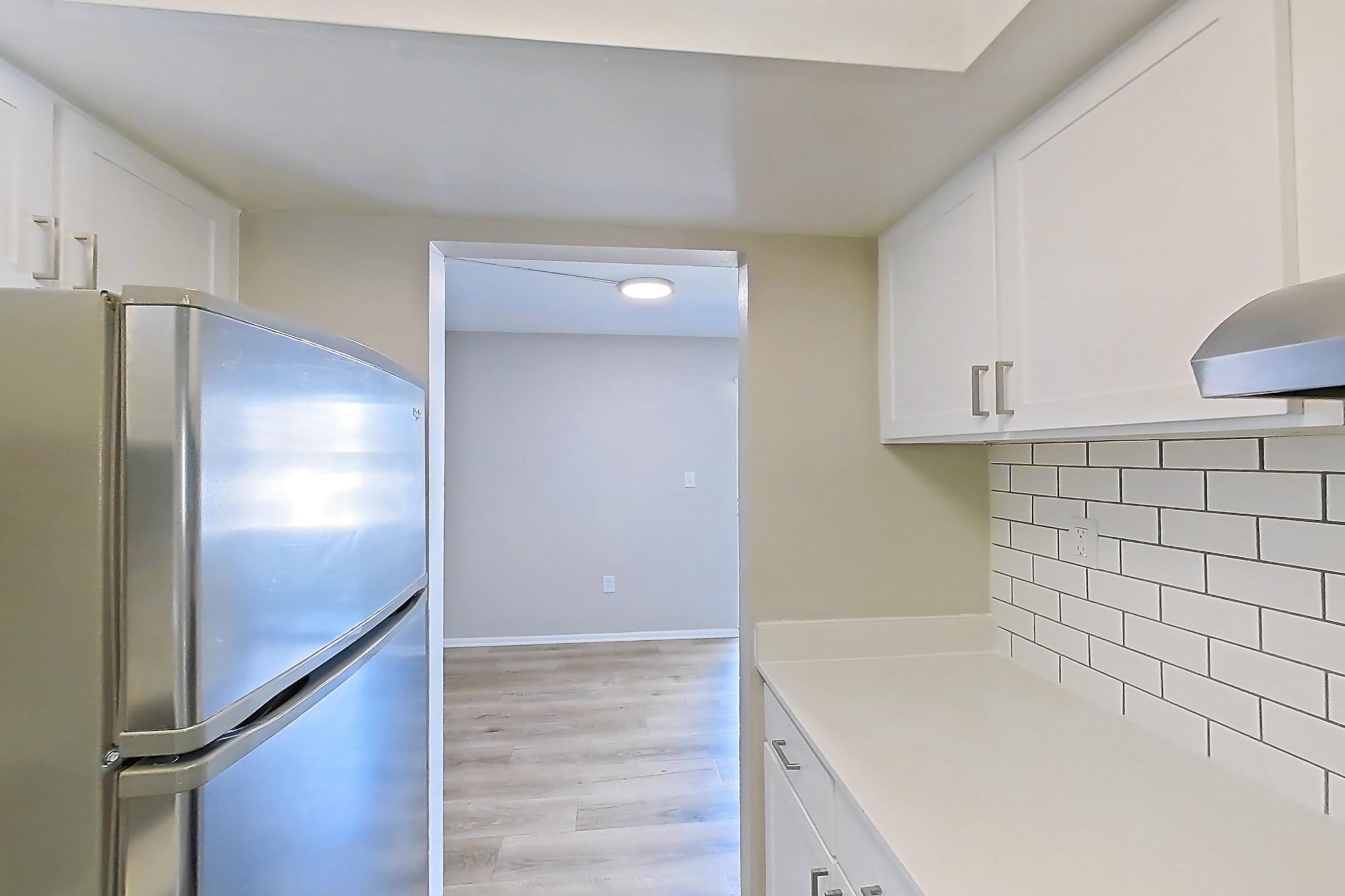 Kitchen with dishwasher, electric range, light countertops, light wood-finish flooring, oven/range, range hood, refrigerator, and stainless steel appliances, Apartment 172 at Venue at Winter Park