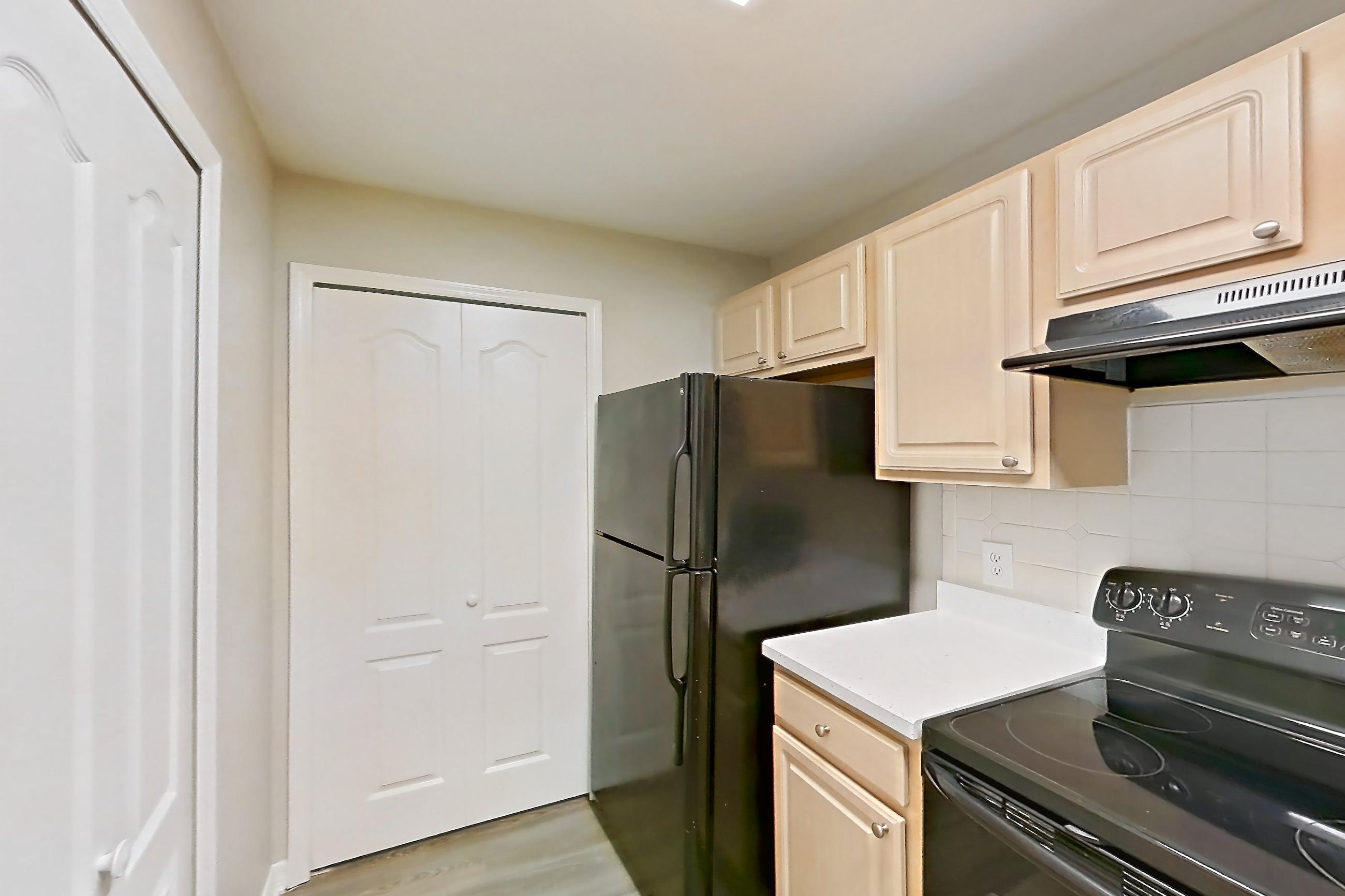 Kitchen with black appliances, dishwasher, electric range, light countertops, light stone countertops, light wood-finish flooring, oven/range, range hood, and refrigerator, Apartment 05-205 at Boot Ranch