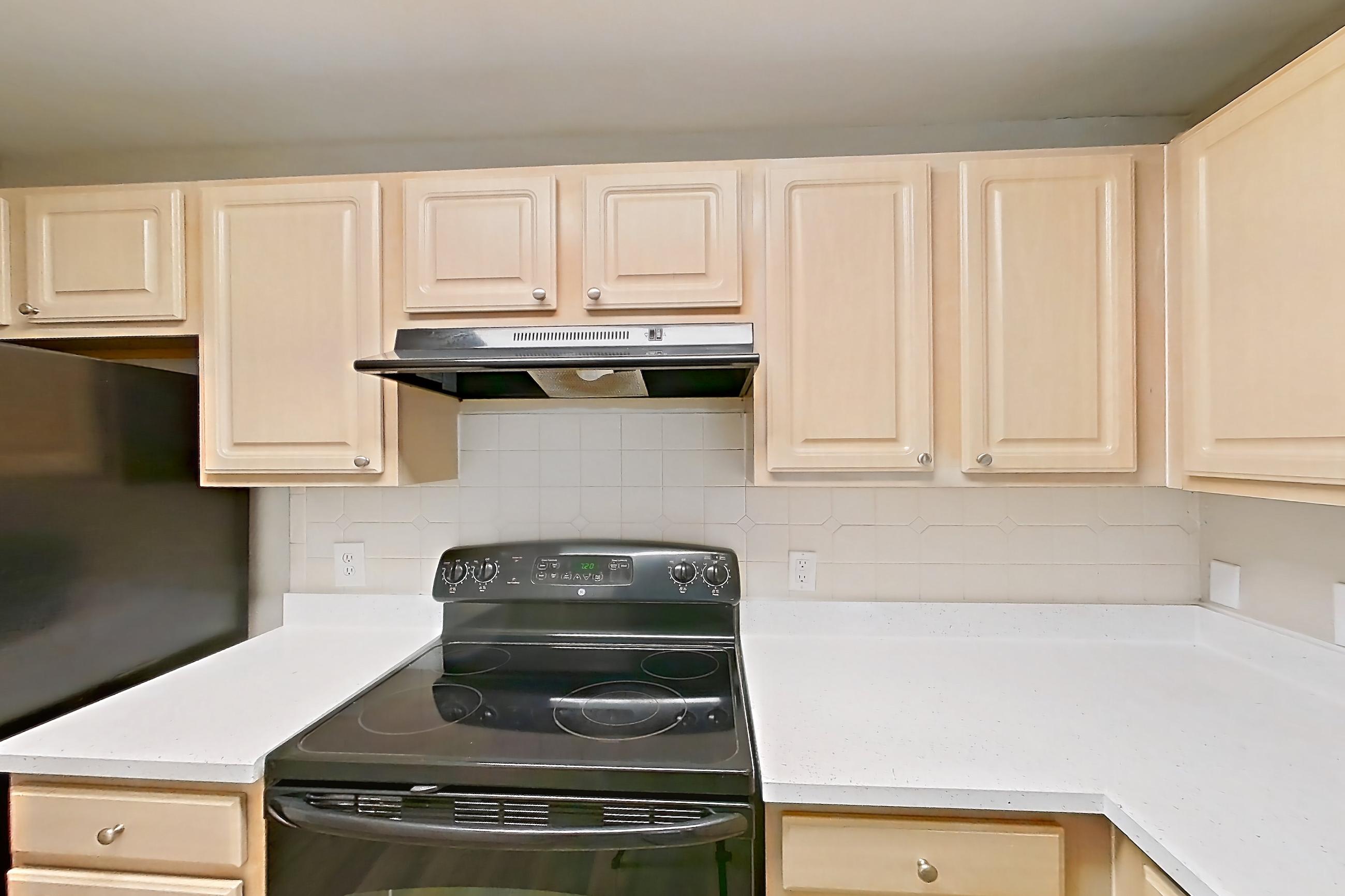 Kitchen with black appliances, dishwasher, electric range, light countertops, light stone countertops, light wood-finish flooring, oven/range, range hood, and refrigerator, Apartment 05-205 at Boot Ranch