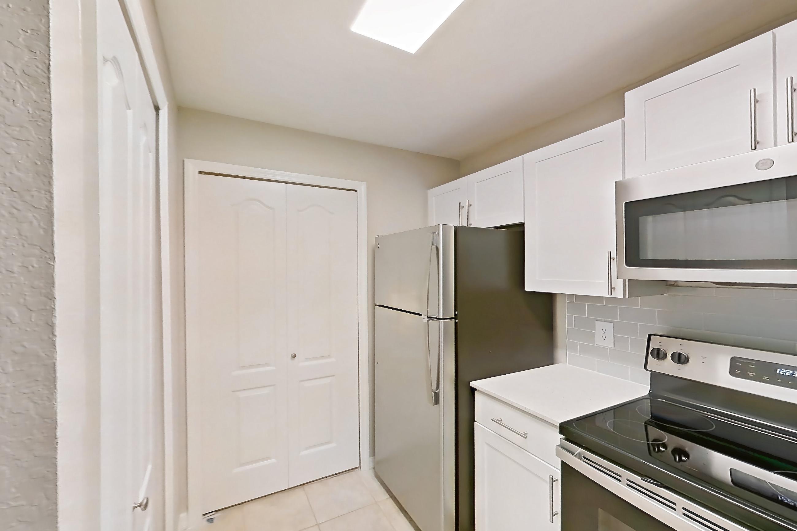 Kitchen with dishwasher, electric range, light countertops, light stone countertops, light tile flooring, light wood-finish flooring, microwave, oven/range, refrigerator, and stainless steel appliances, Apartment 07-204 at Boot Ranch