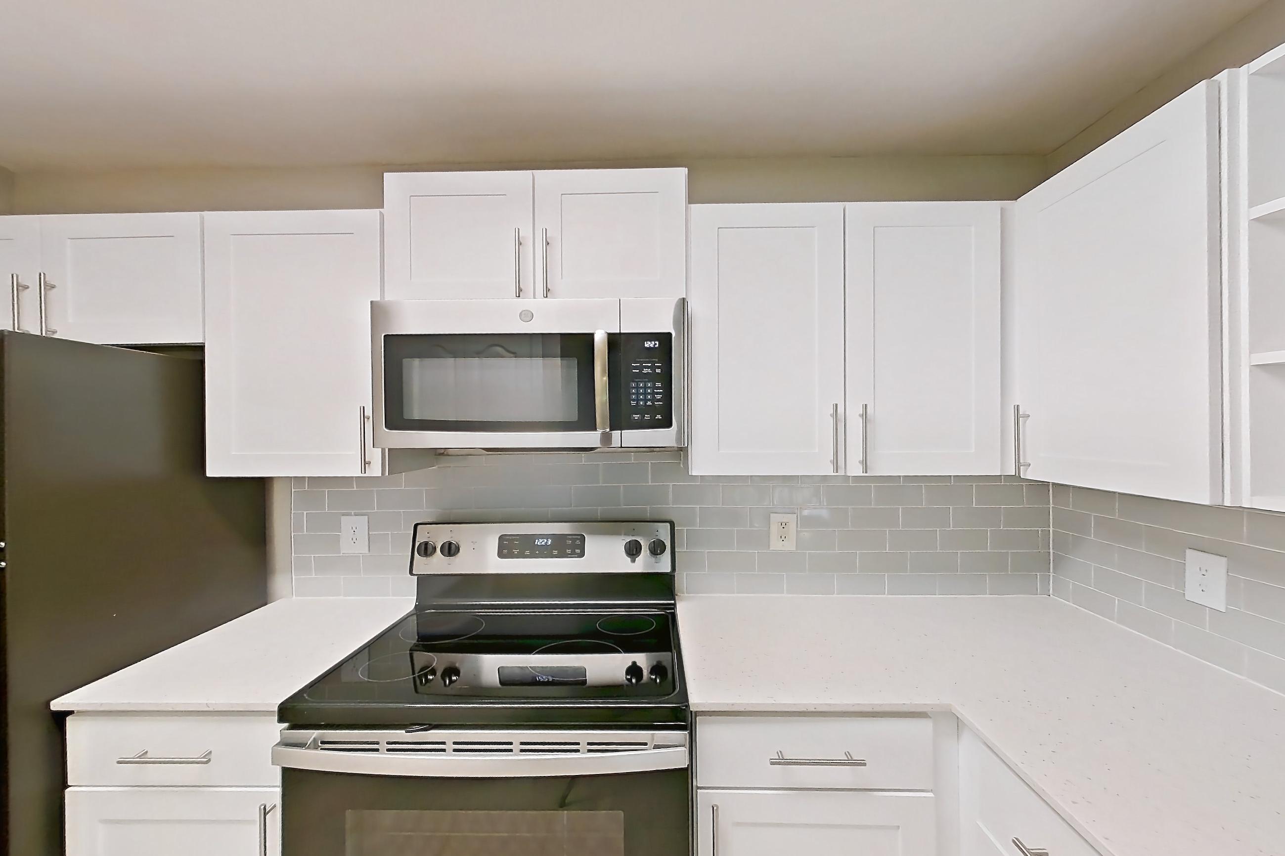 Kitchen with dishwasher, electric range, light countertops, light stone countertops, light tile flooring, light wood-finish flooring, microwave, oven/range, refrigerator, and stainless steel appliances, Apartment 07-204 at Boot Ranch