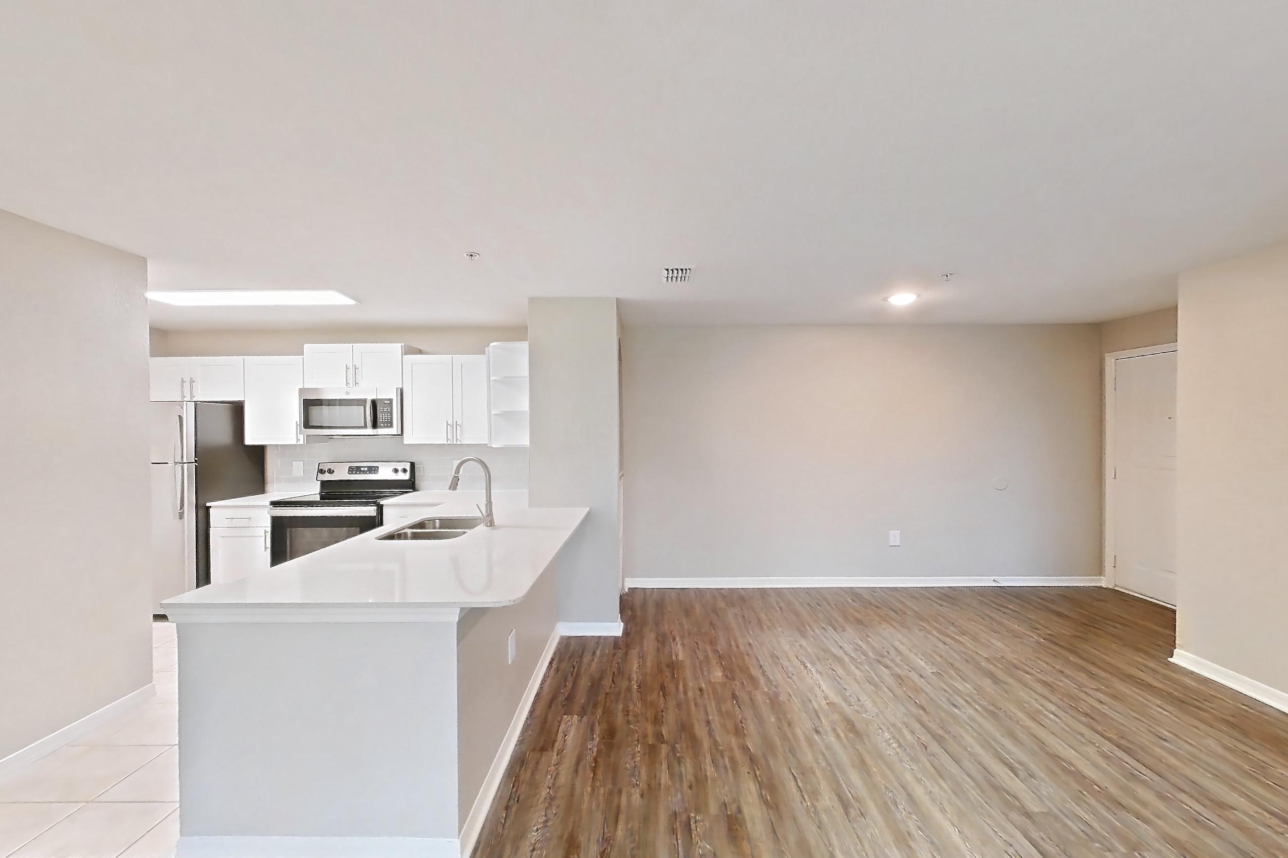 Living space with dark wood-finish flooring, electric range, light countertops, light stone countertops, light wood-finish flooring, oven/range, refrigerator, stainless steel appliances, and white appliances, Apartment 07-204 at Boot Ranch