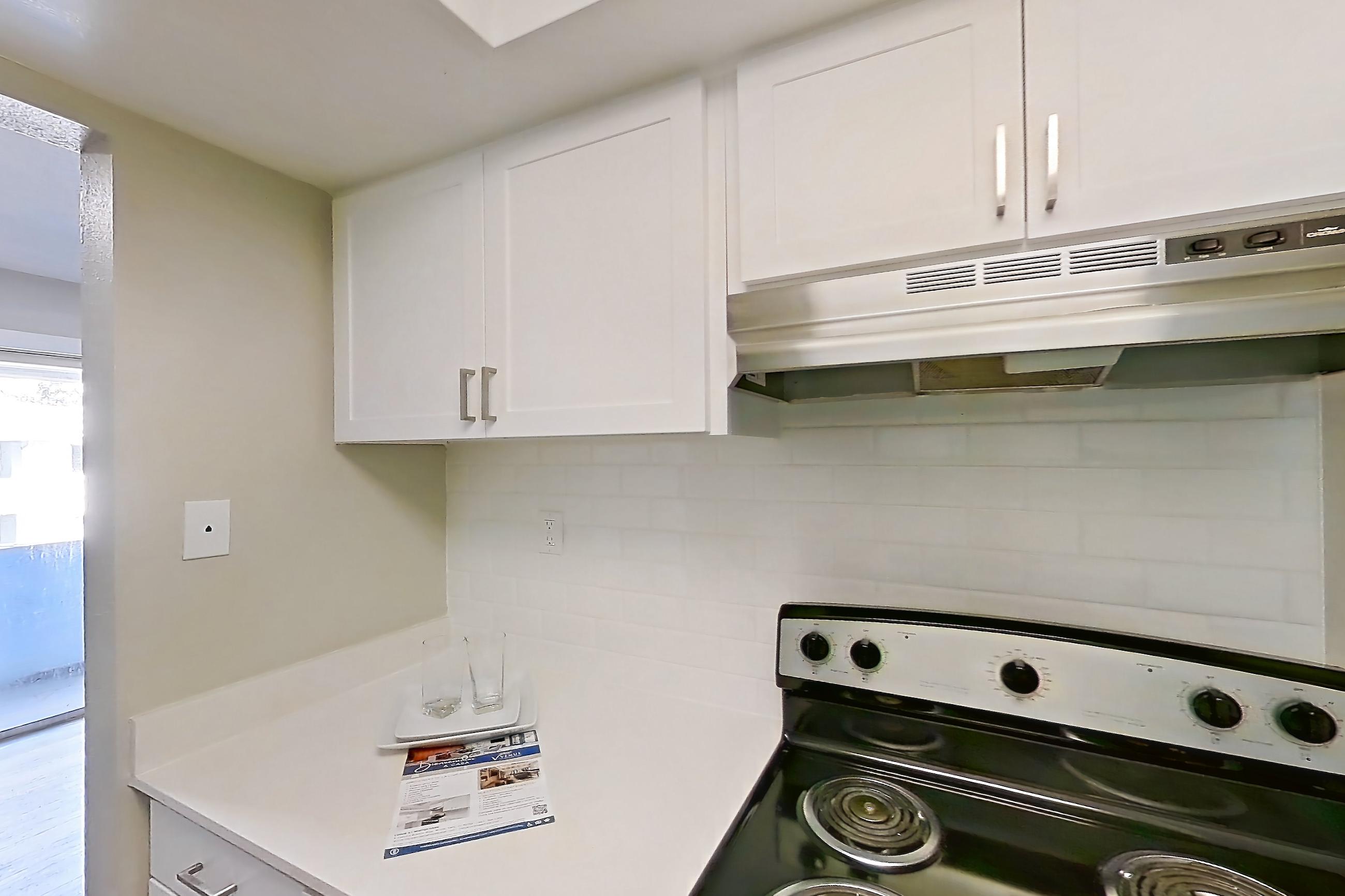 Kitchen with black appliances, dishwasher, electric range, light countertops, light wood-finish flooring, oven/range, range hood, and stainless steel appliances, Apartment 232 at Venue at Winter Park