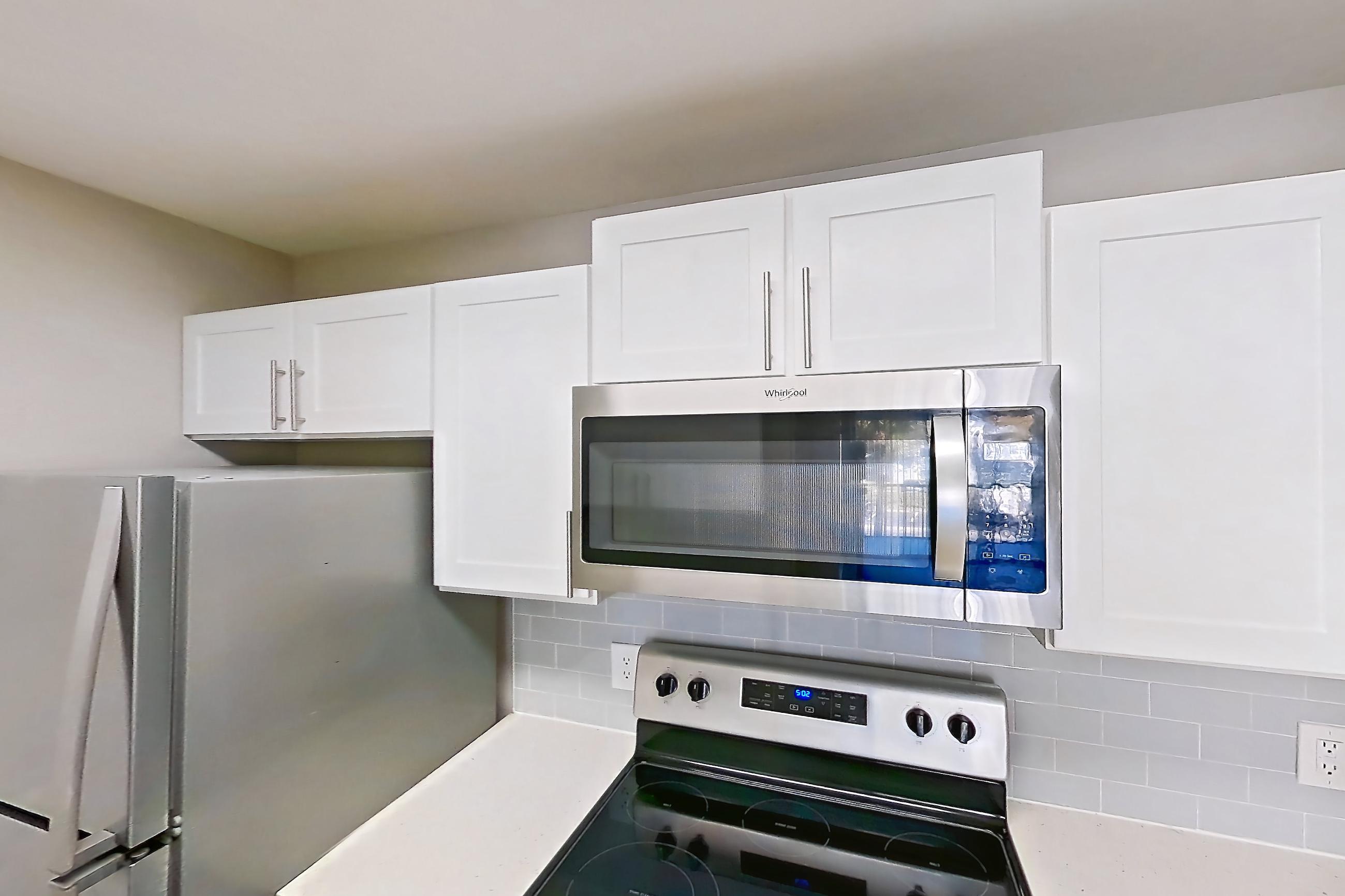 Kitchen with dishwasher, electric range, light countertops, light stone countertops, light wood-finish flooring, microwave, oven/range, refrigerator, and stainless steel appliances, Apartment 09-201 at Boot Ranch